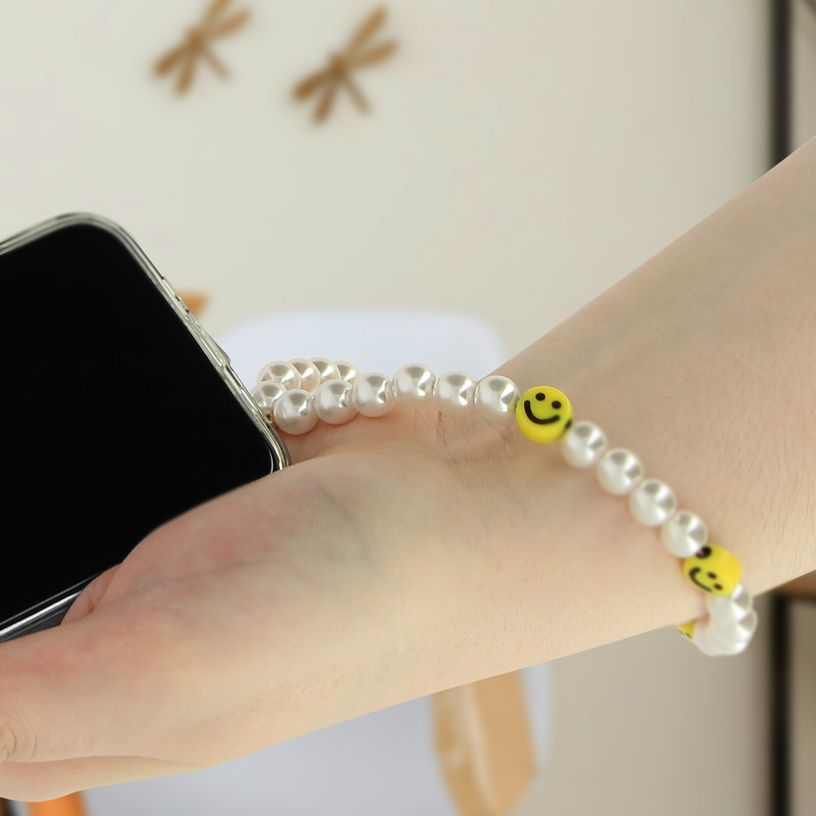 Un polso indossa un braccialetto di perle con perline a faccina sorridente gialla. Un telefono nell'altra mano.