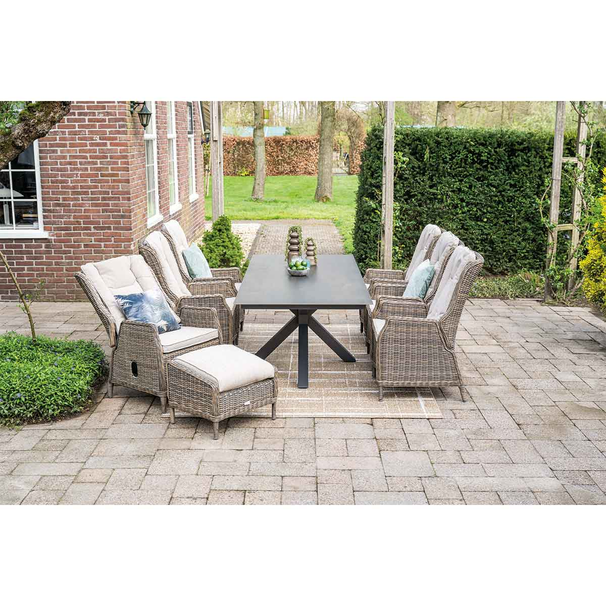 Wicker terrasmeubilair met donkere tafel en stoelen op stenen terras, bakstenen huis op achtergrond.