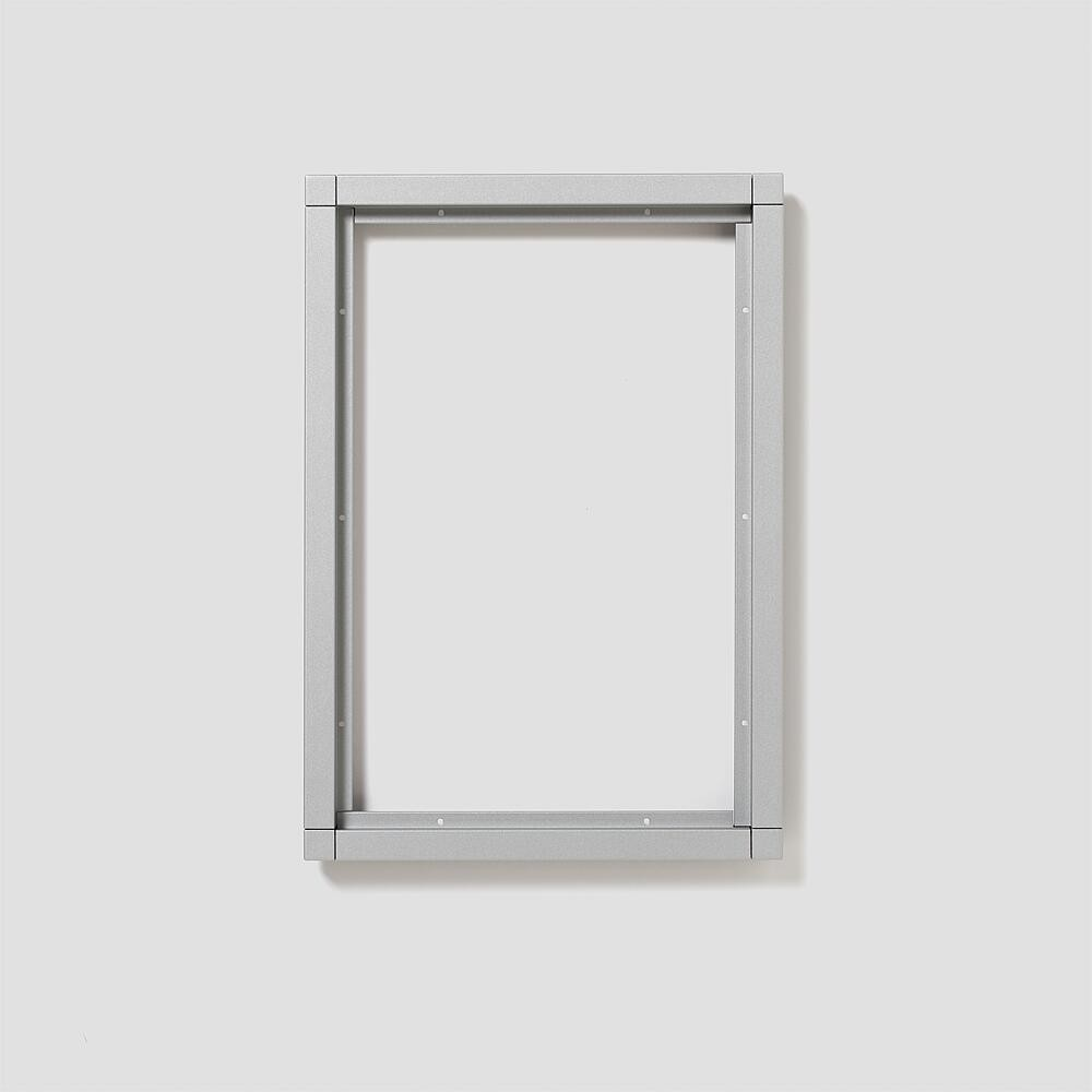 Una semplice cornice argentata con viti a vista su sfondo grigio chiaro.