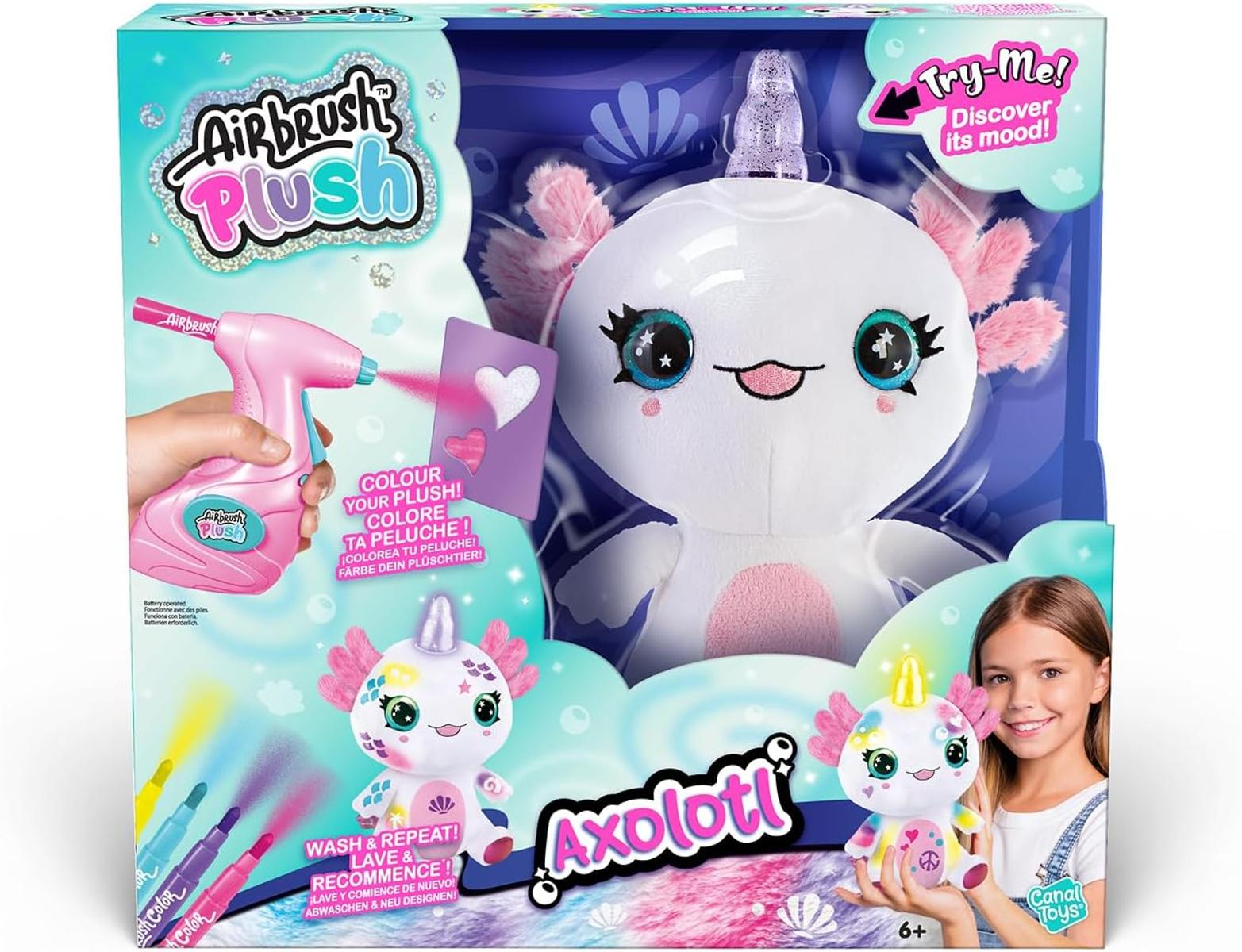 Un axolotl di peluche bianco con branchie rosa e corno glitterato, in scatola con pistola spray e pennarelli.