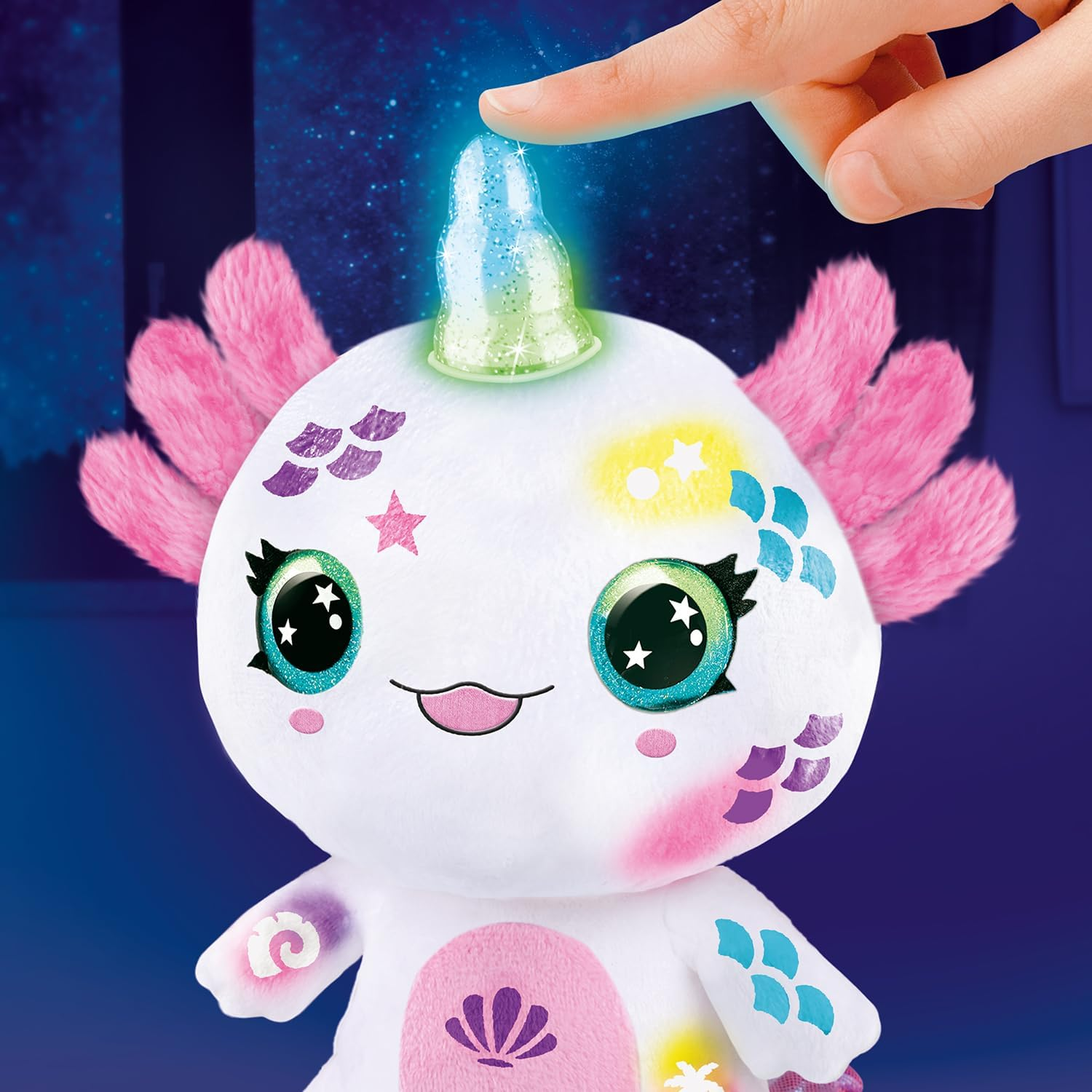Il dito di una persona tocca un corno luminoso su un peluche bianco con pinne rosa e segni colorati.