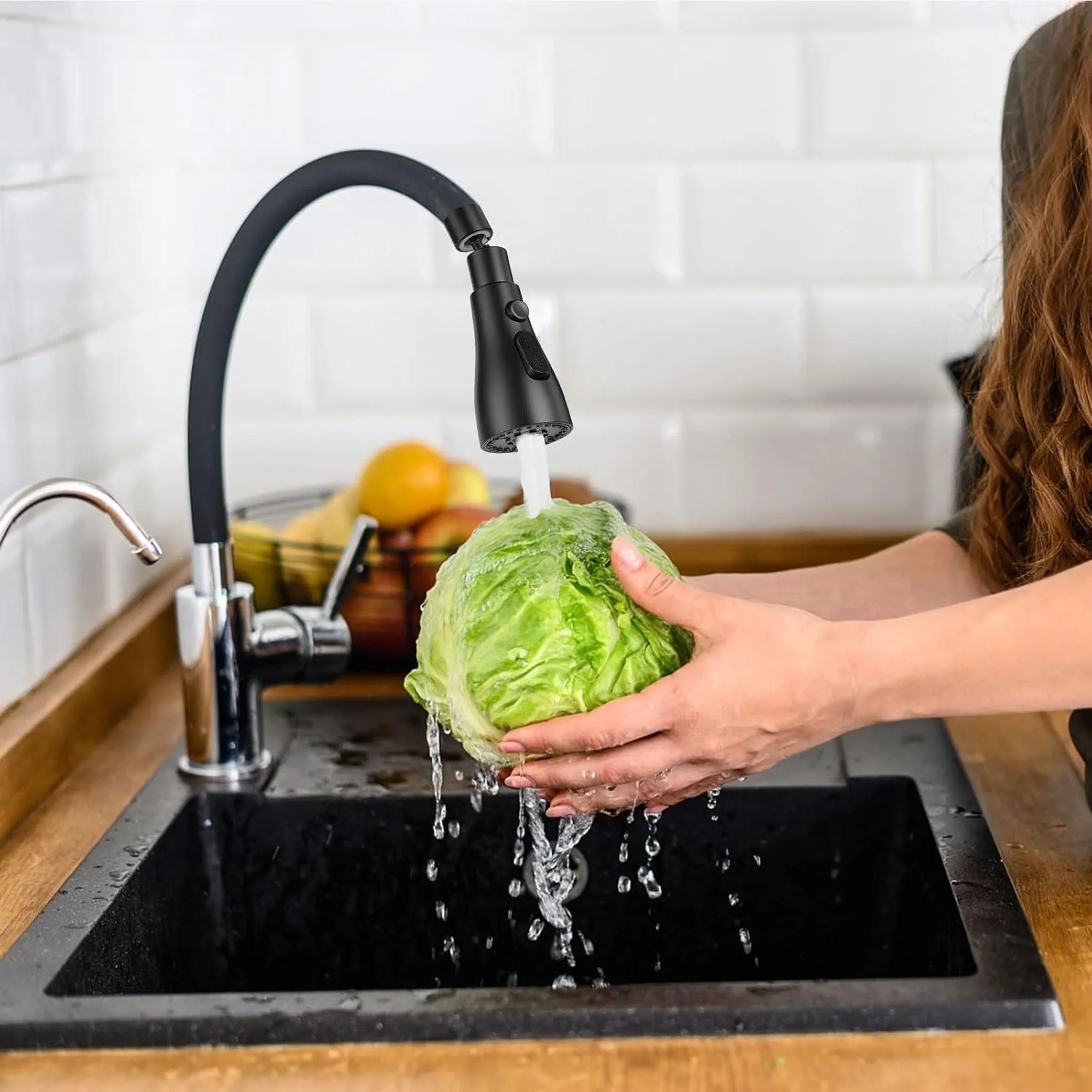 Eine Person wäscht einen grünen Kopfsalat unter fließendem Wasser in einer schwarzen Spüle.
