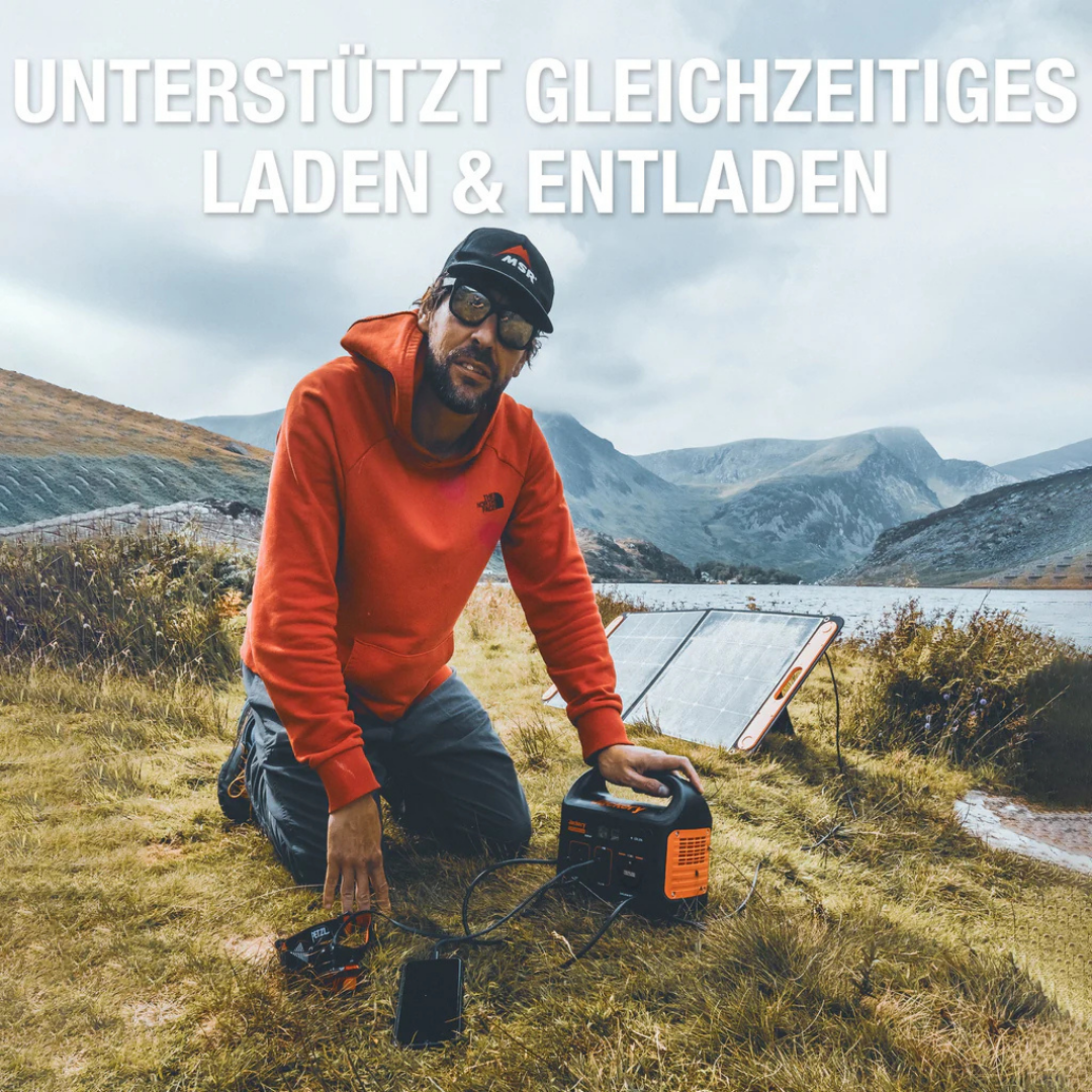 Mann kniet mit Solar-Ladegerät, Powerbank, Handy und Solarpanel in malerischer Landschaft.