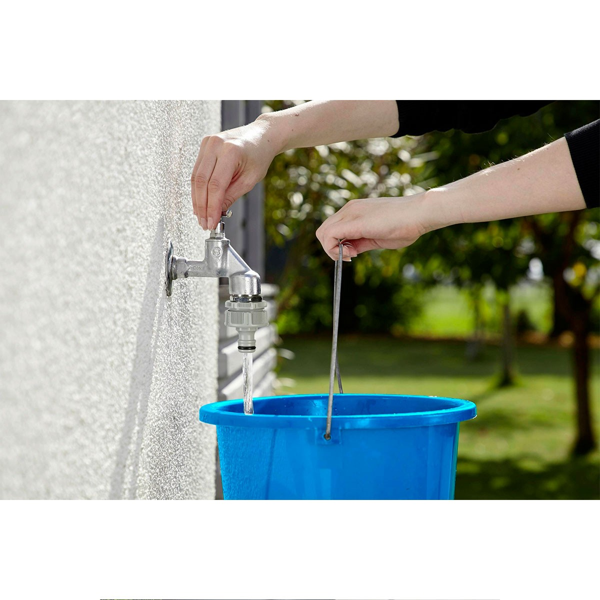 Persona che riempie secchio blu con acqua da rubinetto su muro casa.