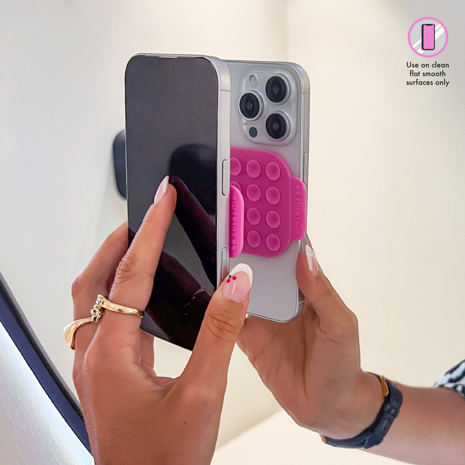 Mani che tengono un iPhone argentato con impugnatura rosa. Si riflette un telefono scuro.