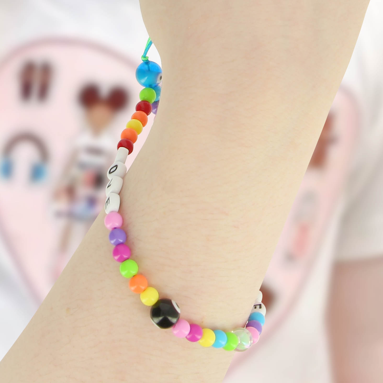 Un braccialetto di perline arcobaleno con lettere "LOVE" e un ciondolo occhio malvagio nero su un polso.