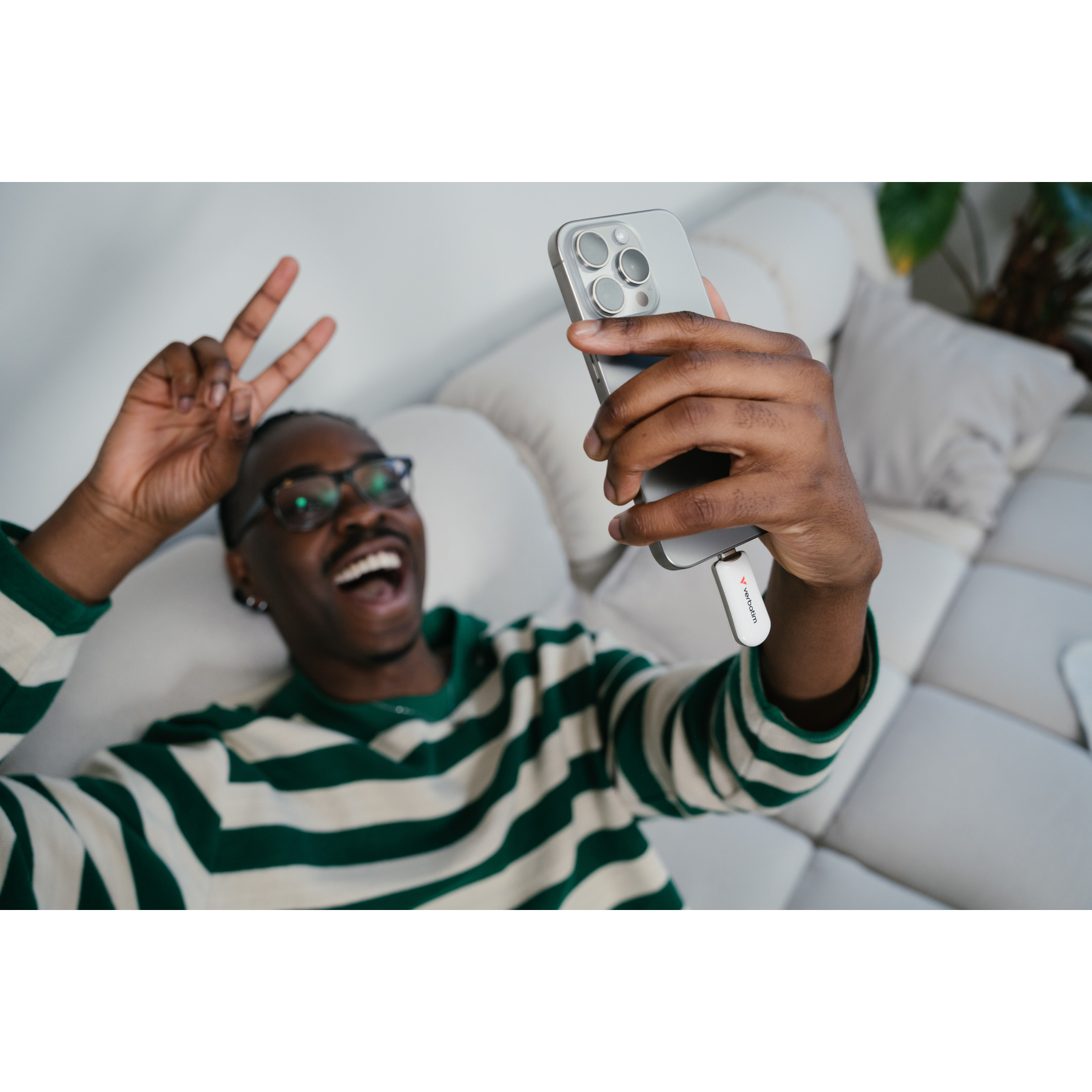 Mężczyzna w zielono-białej bluzce w paski robi selfie, trzyma telefon i pokazuje znak pokoju.