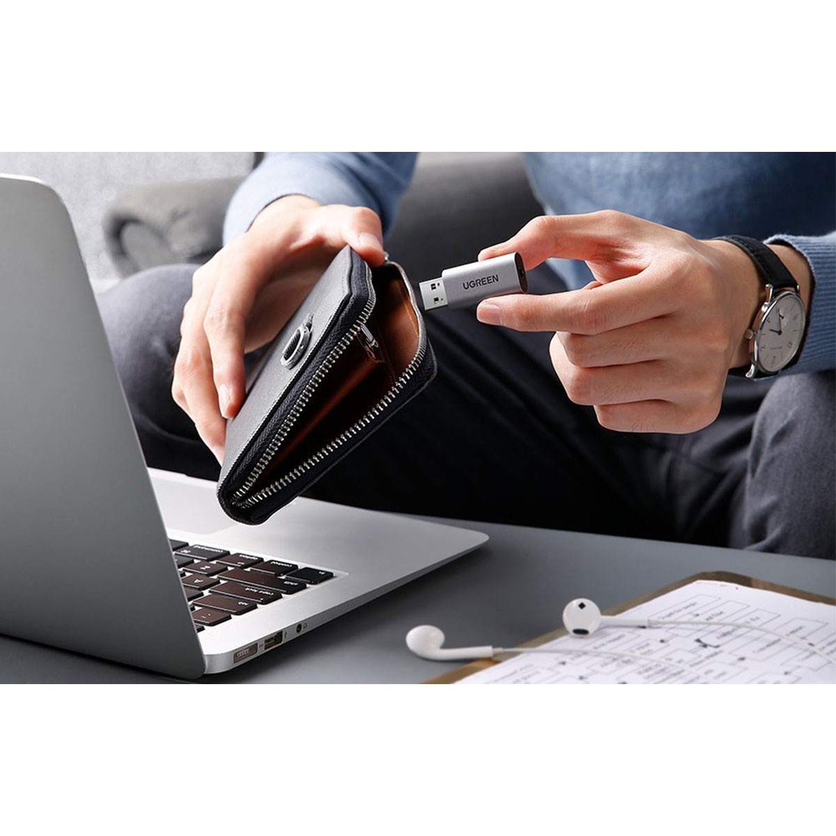 Osoba trzymająca pendrive UGREEN i portfel nad laptopem.