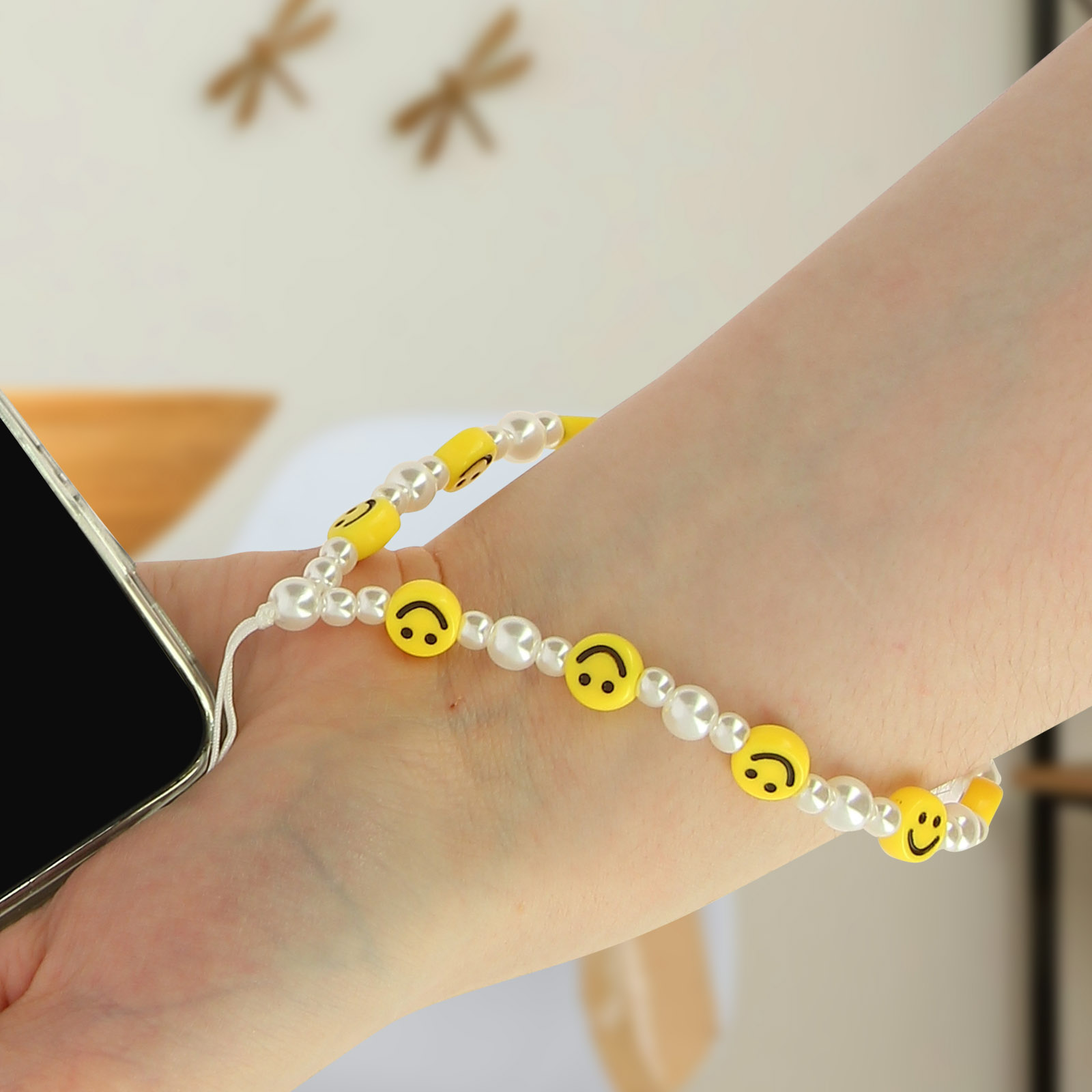Una mano tiene uno smartphone con una catena di perline con faccine sorridenti attaccate.