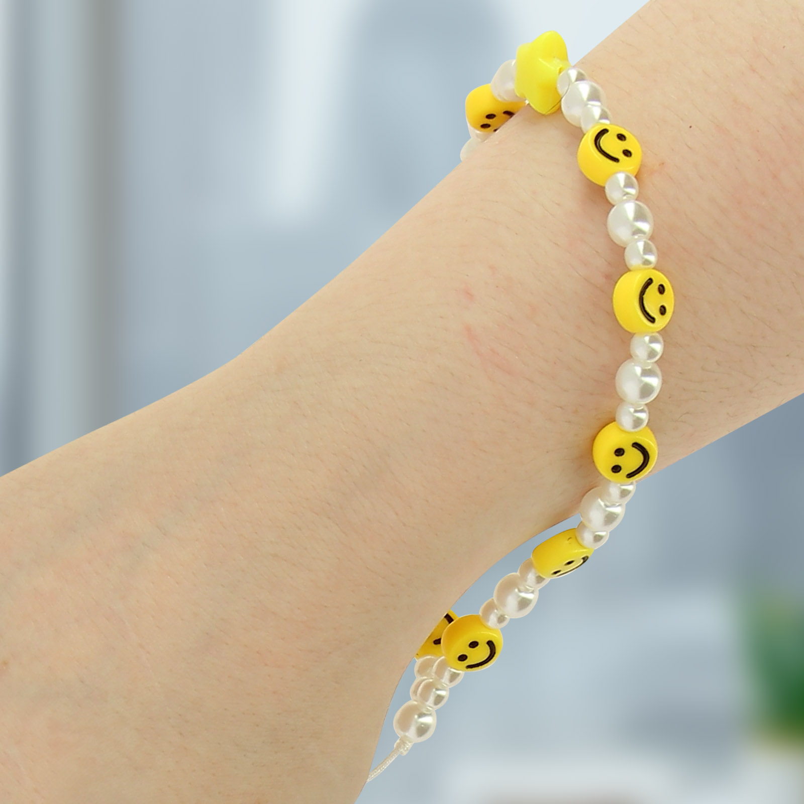 Braccialetto con perle bianche e perline gialle sorridenti indossato su un braccio.