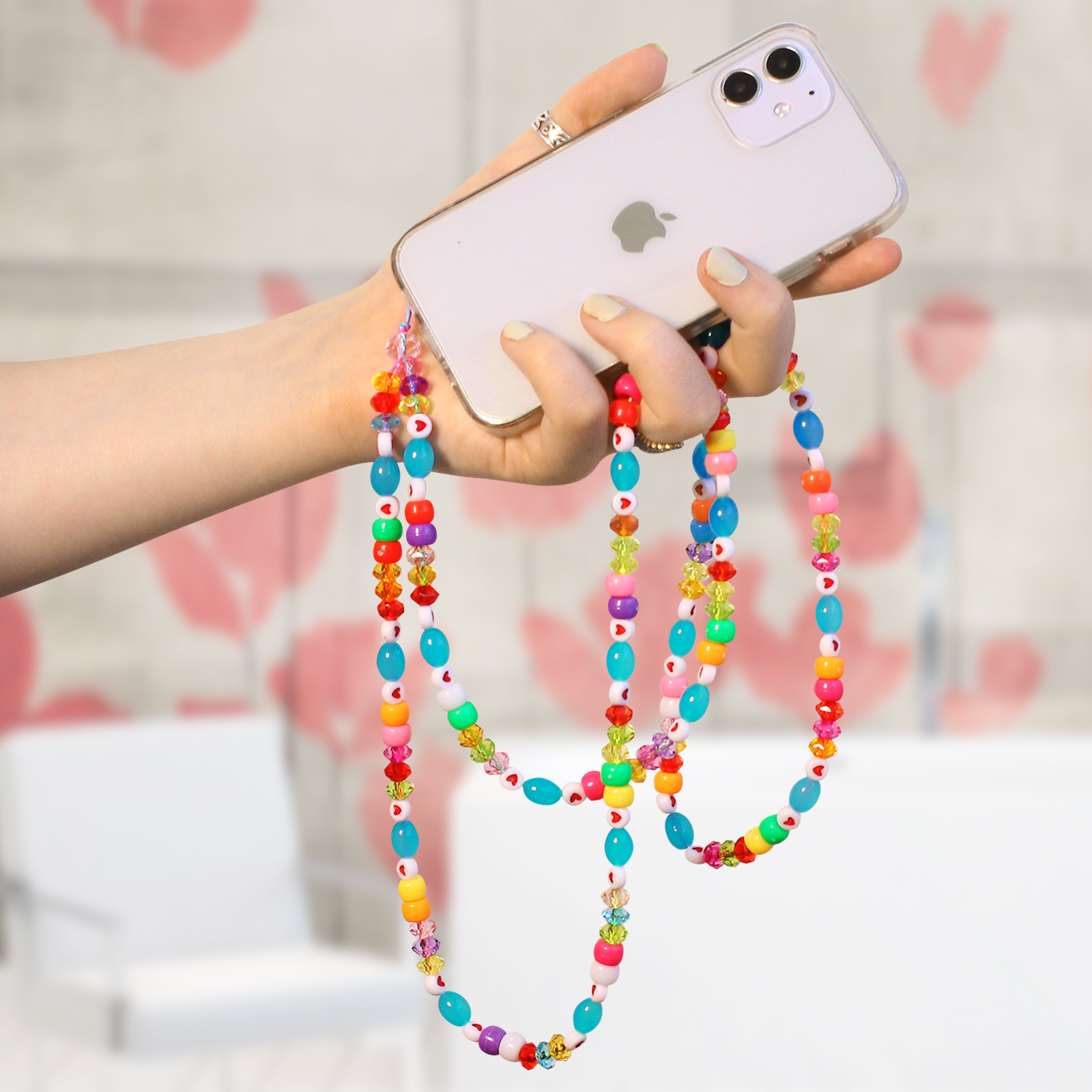 Una mano tiene un telefono con un cinturino di perline colorate con cuori, stelle e varie forme.