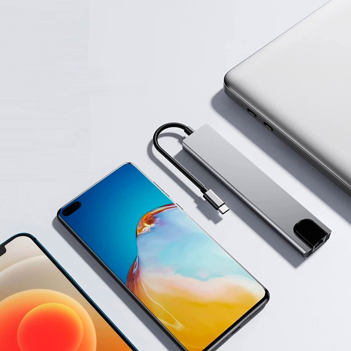 Eine silberne USB-C-Dockingstation verbindet ein Handy und einen Laptop. Zwei Handys sind sichtbar.