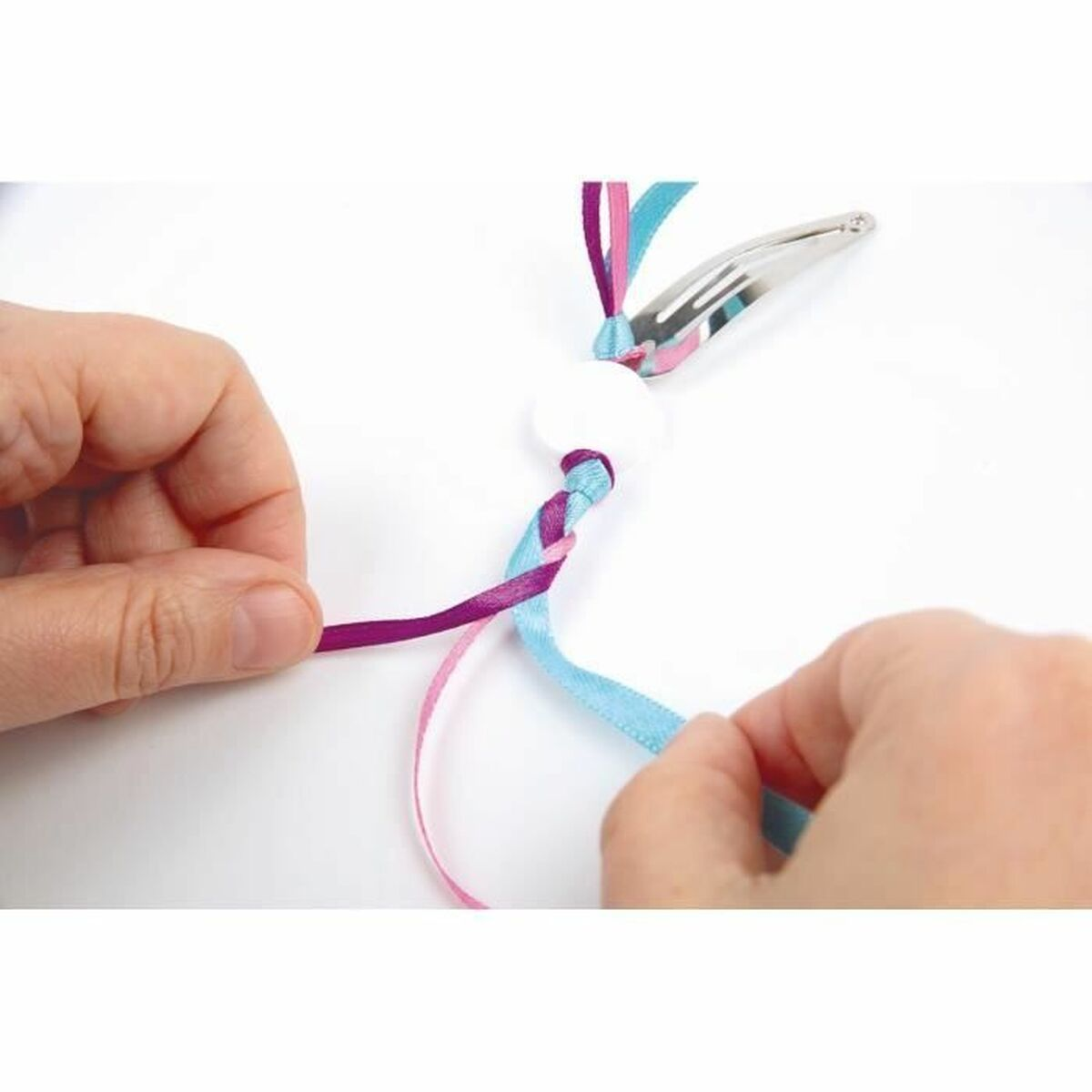Mani intrecciano nastri rosa, viola e blu attaccati a una molletta d'argento.