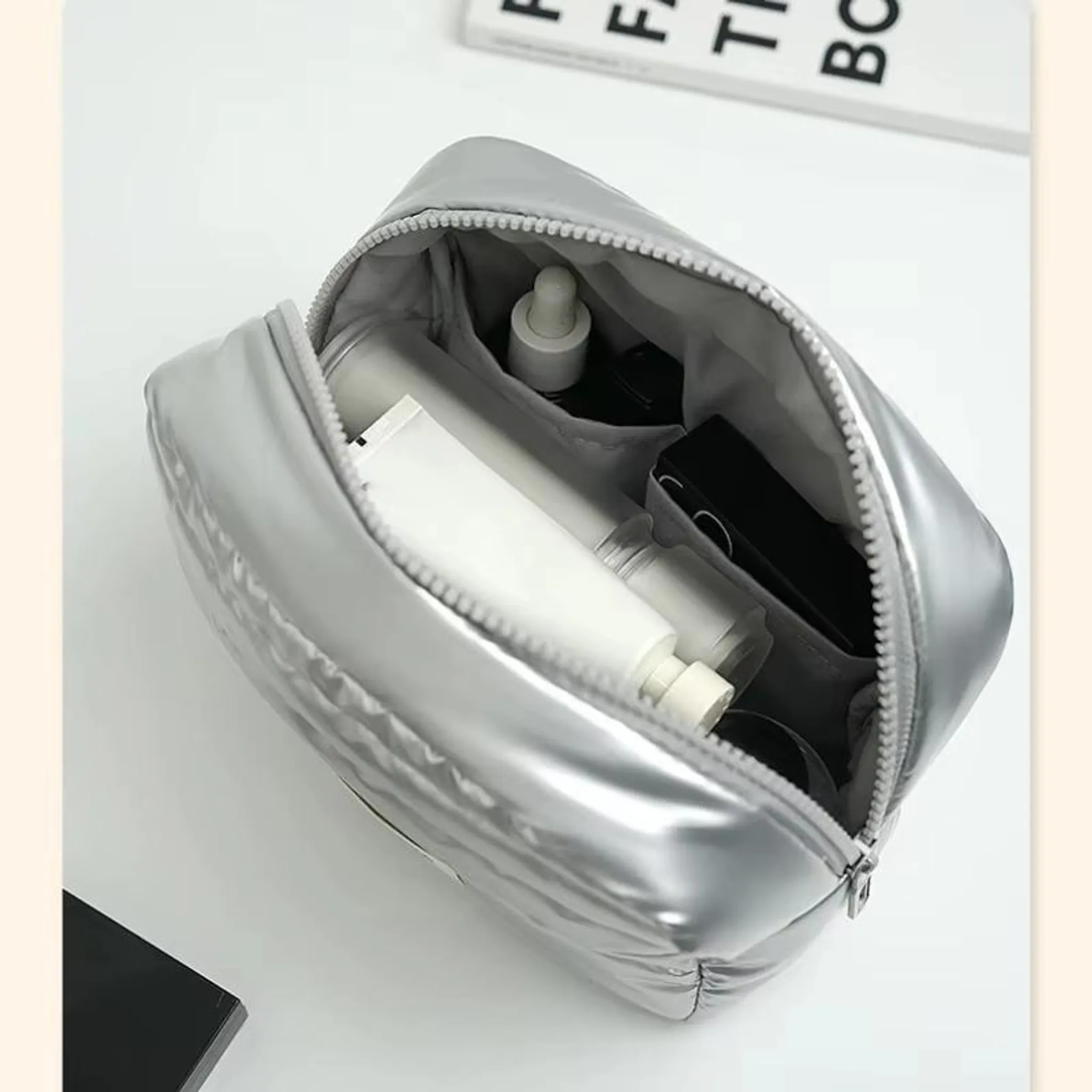 Silberne Kosmetiktasche mit Reißverschluss, gefüllt mit Tuben und Flaschen.