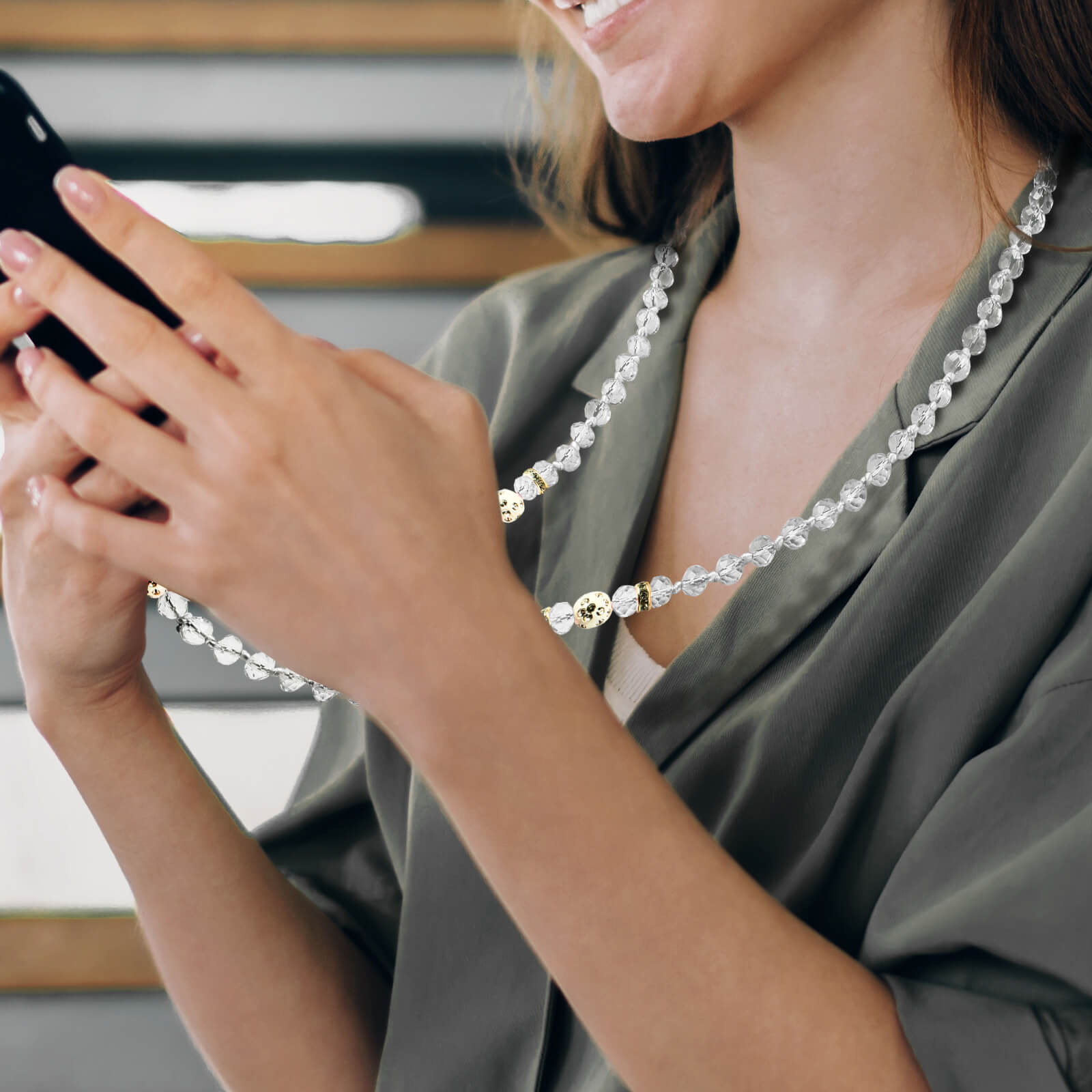 Una donna che tiene uno smartphone con una collana di perle al collo.