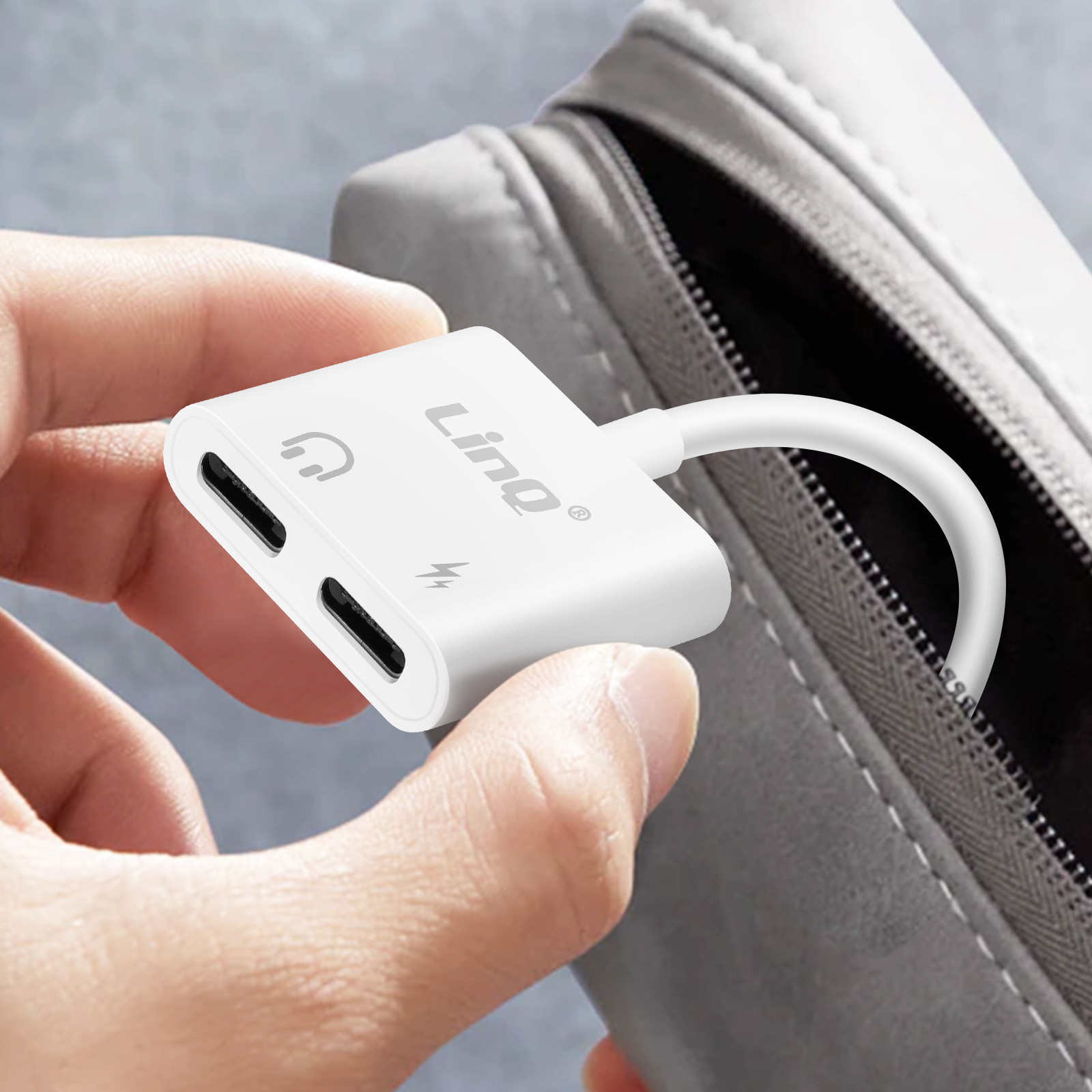 Adattatore USB-C bianco con icone cuffie e ricarica, tenuto davanti a una borsa.