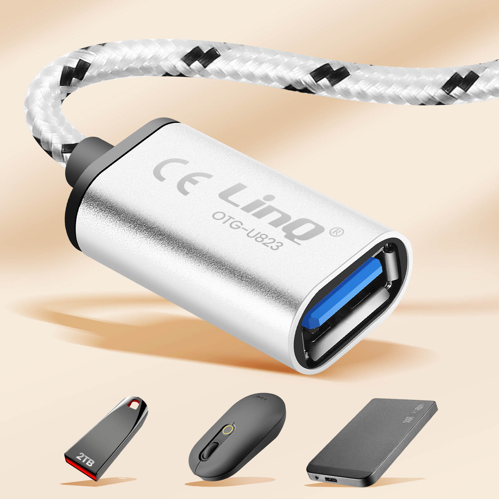 Un adattatore USB-C argentato con cavo intrecciato è mostrato sopra un'unità flash da 2 TB, un mouse e un hard disk esterno.