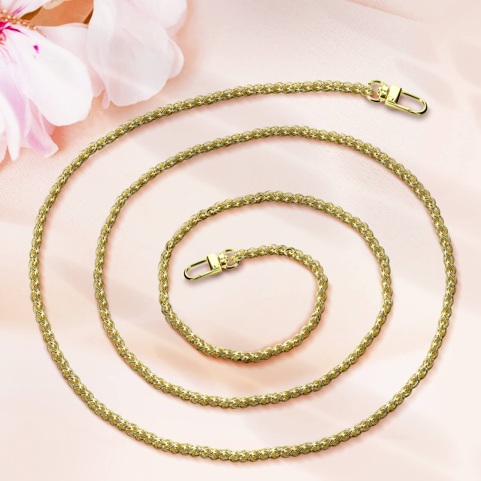 Una catena d'oro con due chiusure giace su uno sfondo di tessuto rosa con fiori rosa tenui.