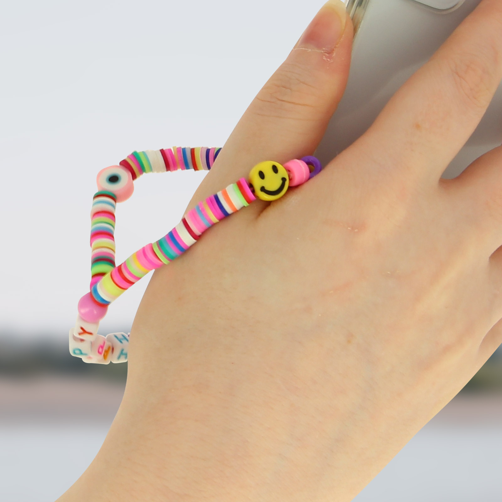 Una mano tiene un telefono con un cinturino di perline colorate con faccina sorridente e occhio.