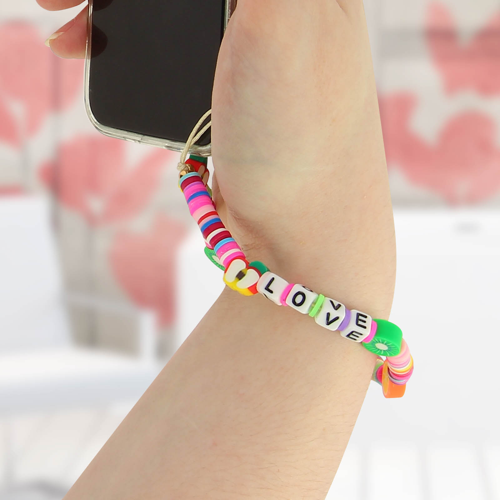 Un braccialetto colorato con perline che compongono la parola 'LOVE' è indossato su un polso che tiene un telefono.