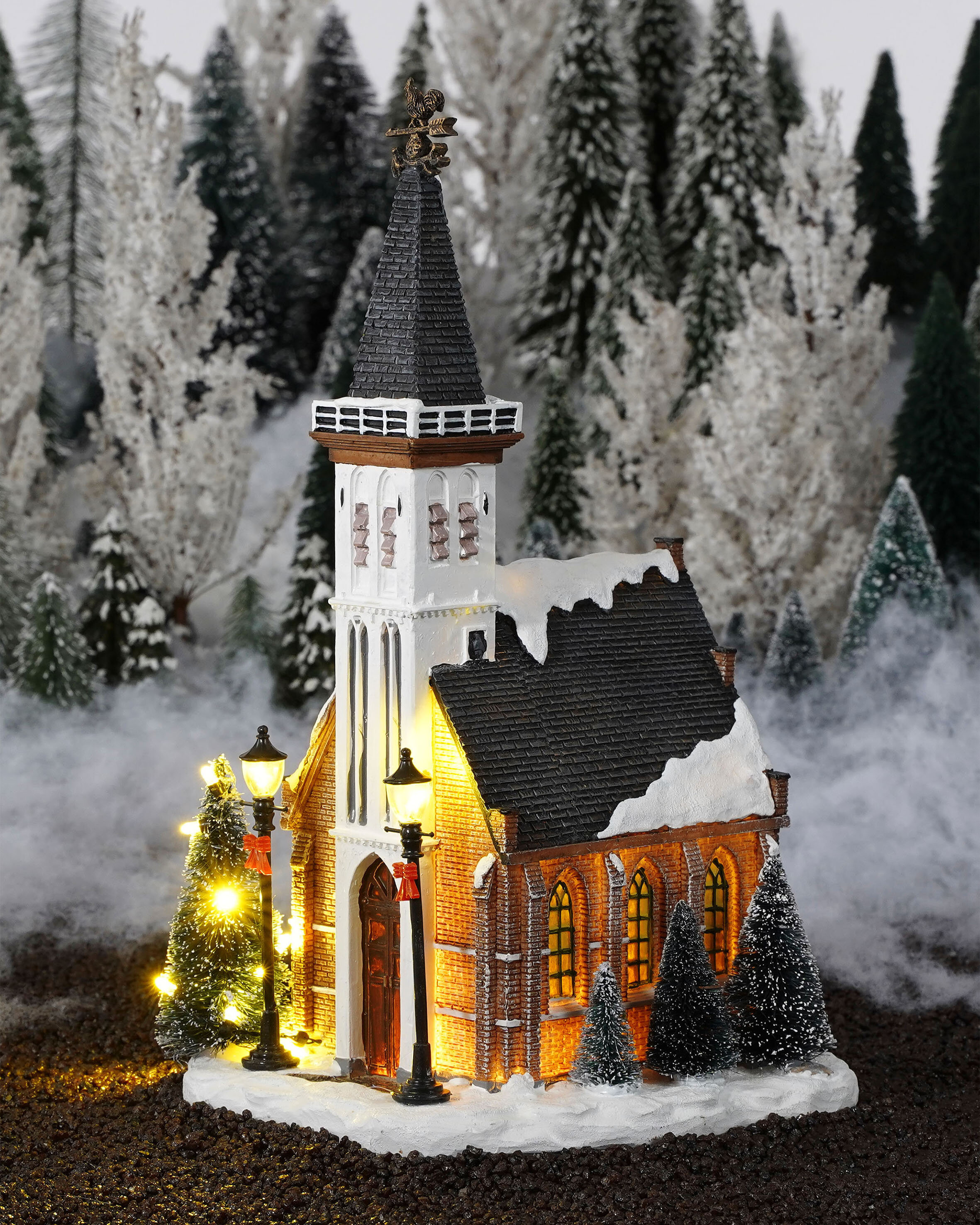 Kerstkerkmodel met sneeuw en verlichte bomen.