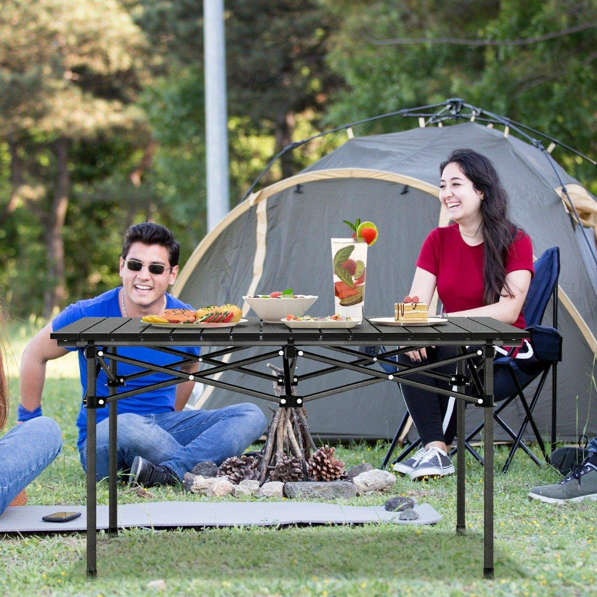 Gente disfrutando una comida en una mesa de picnic con una tienda de campaña al fondo.