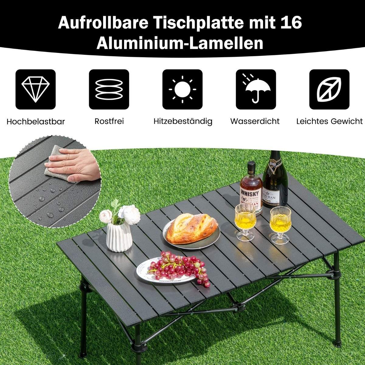 Una mesa plegable de aluminio de listones gris oscuro sobre césped con pan, uvas y bebidas.