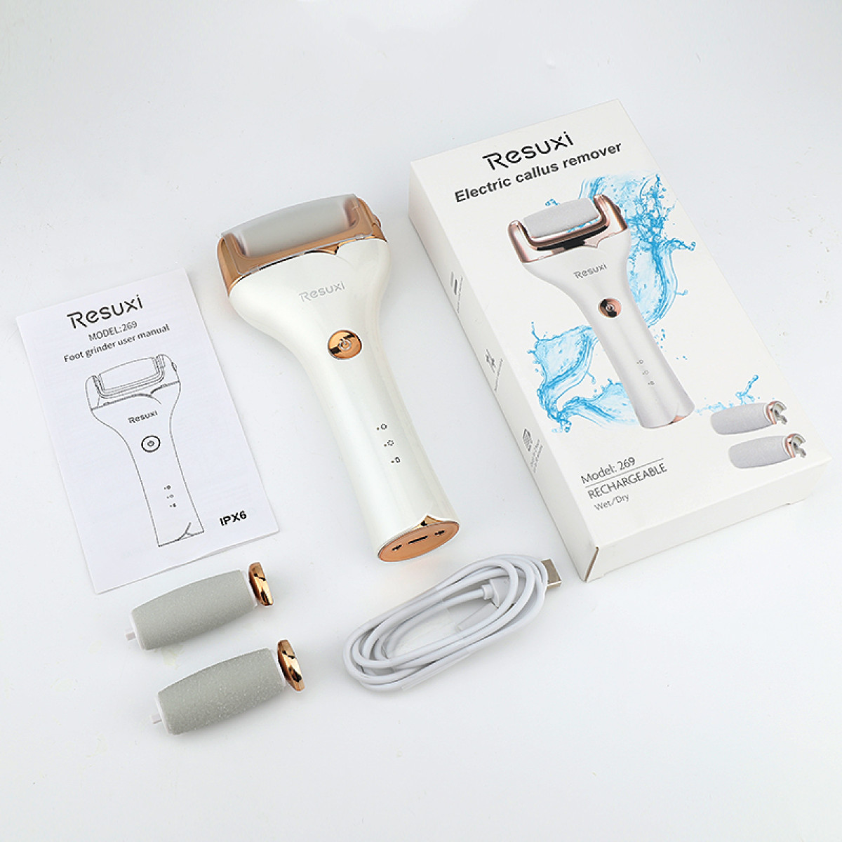 Weißer elektrischer Hornhautentferner mit goldenen Akzenten, Anleitung, USB-Kabel und zwei Ersatzrollen.
