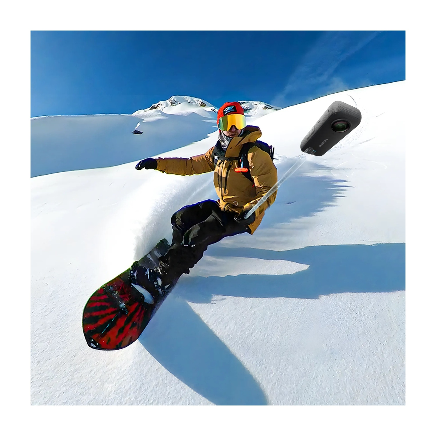 Kamera ile selfie çubuğu tutan snowboardcu, karlı dağda havada.