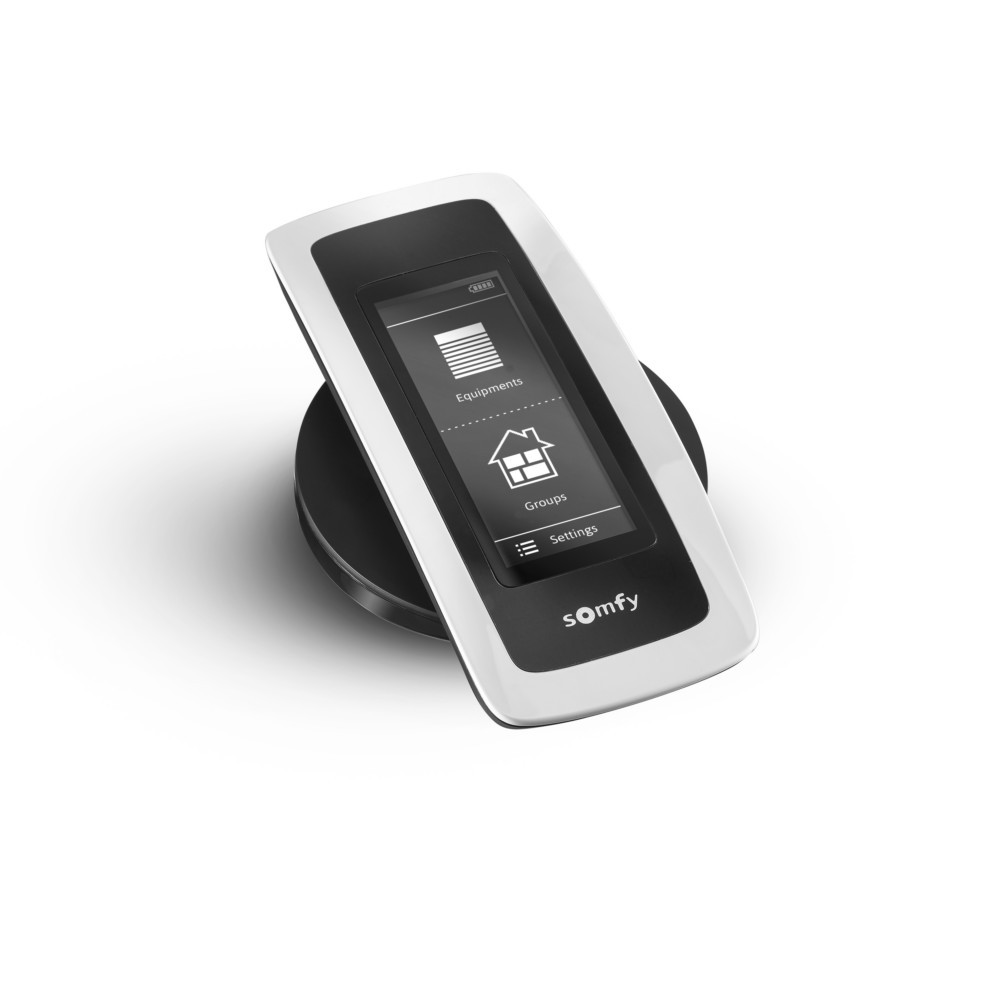 Un telecomando Somfy bianco con base nera mostra "Attrezzature", "Gruppi" e "Impostazioni" sullo schermo.