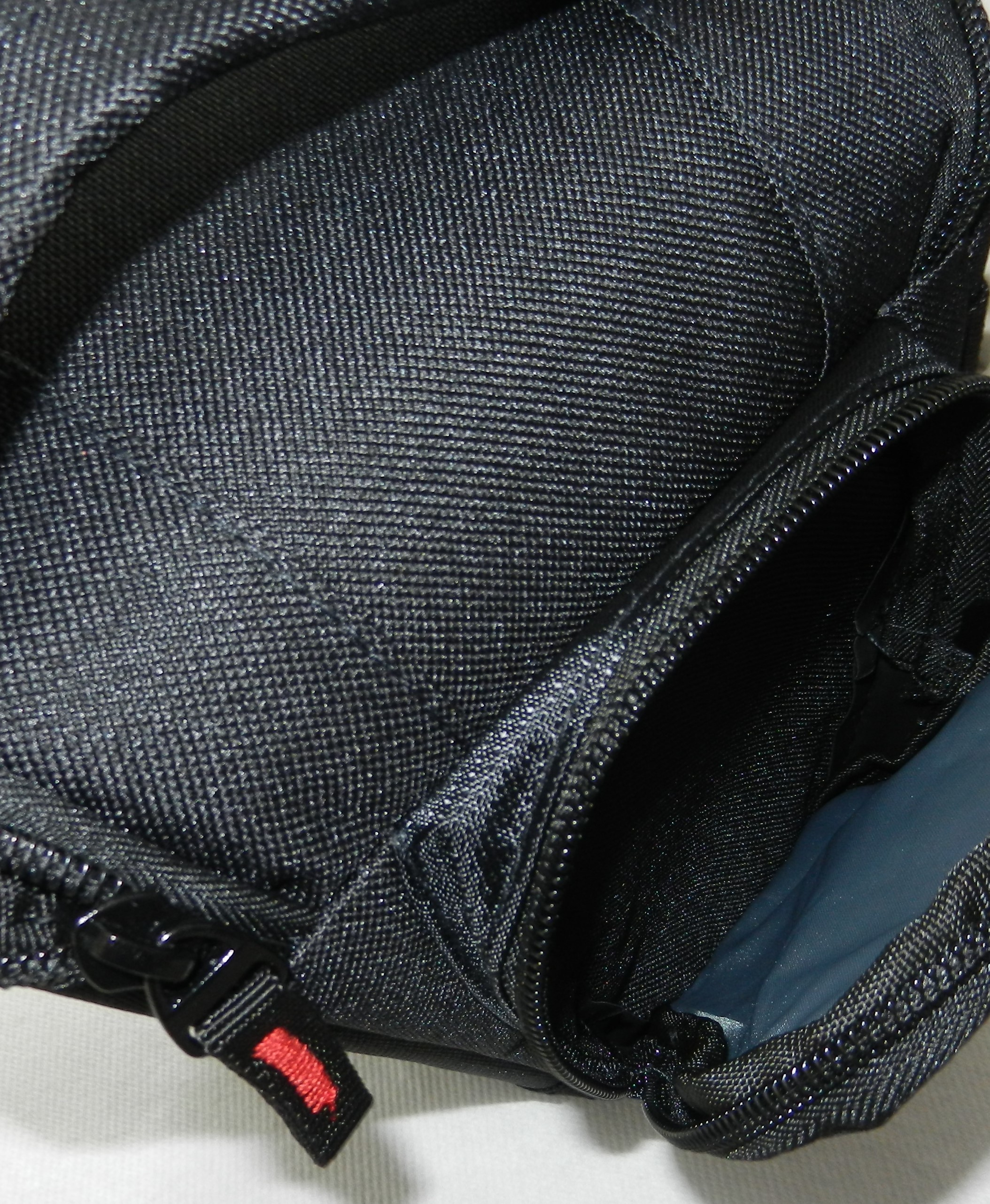 Una borsa nera con cerniera e un dettaglio rosso sul tiretto della cerniera.