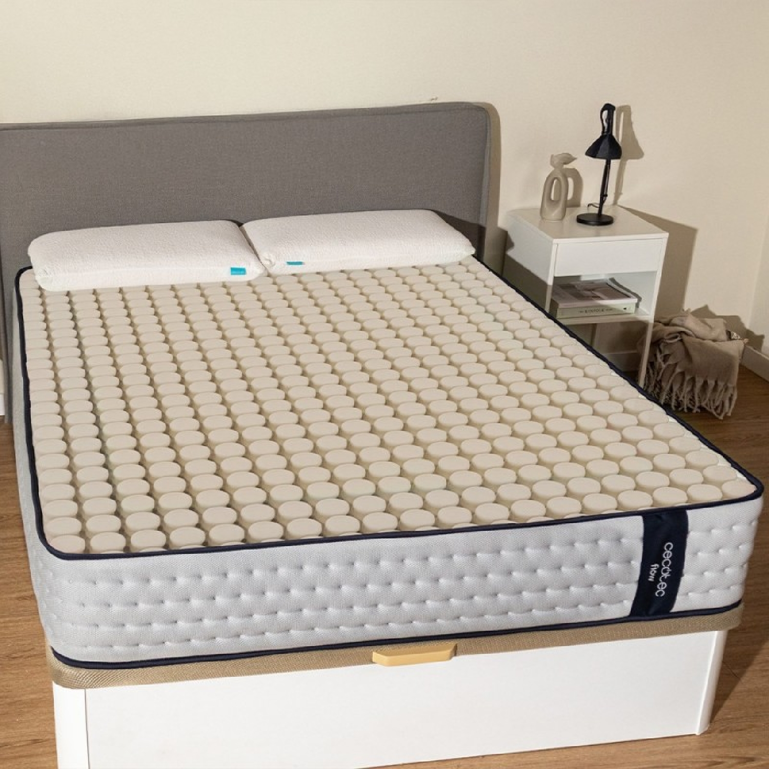 Un colchón blanco y gris con dos almohadas blancas sobre una cama con cabecero gris.
