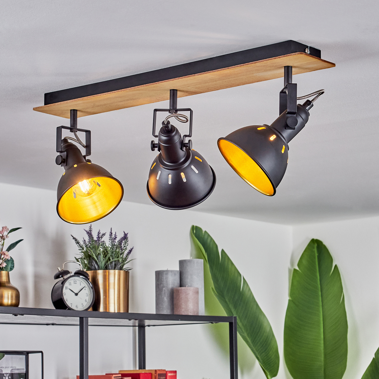 Eine schwarze Schienenleuchte mit drei verstellbaren Strahlern mit goldenem Innenleben auf einer Holzplanke.