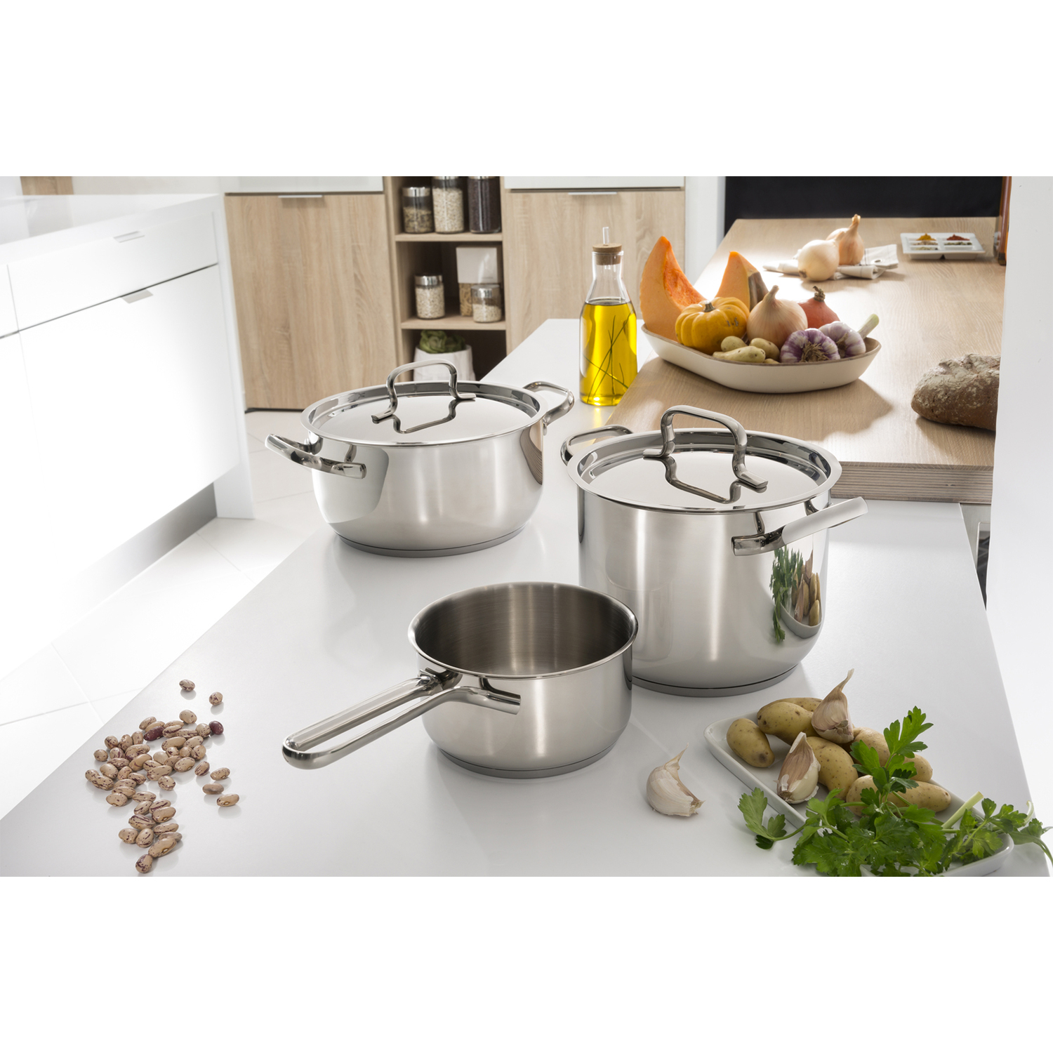 Ollas y sartenes brillantes en una encimera de cocina con verduras como calabaza, cebollas, ajo y patatas.