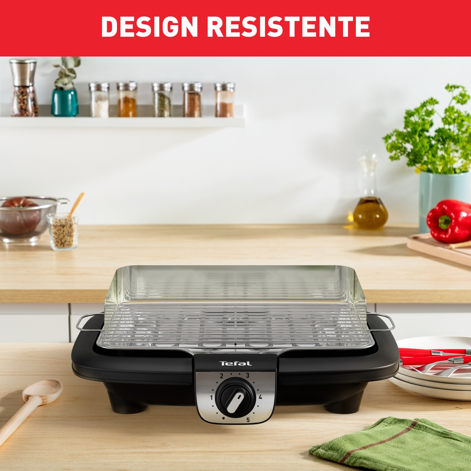 Grill elektryczny Tefal z chromowanym rusztem stoi na drewnianym blacie. Po lewej drewniana łyżka.