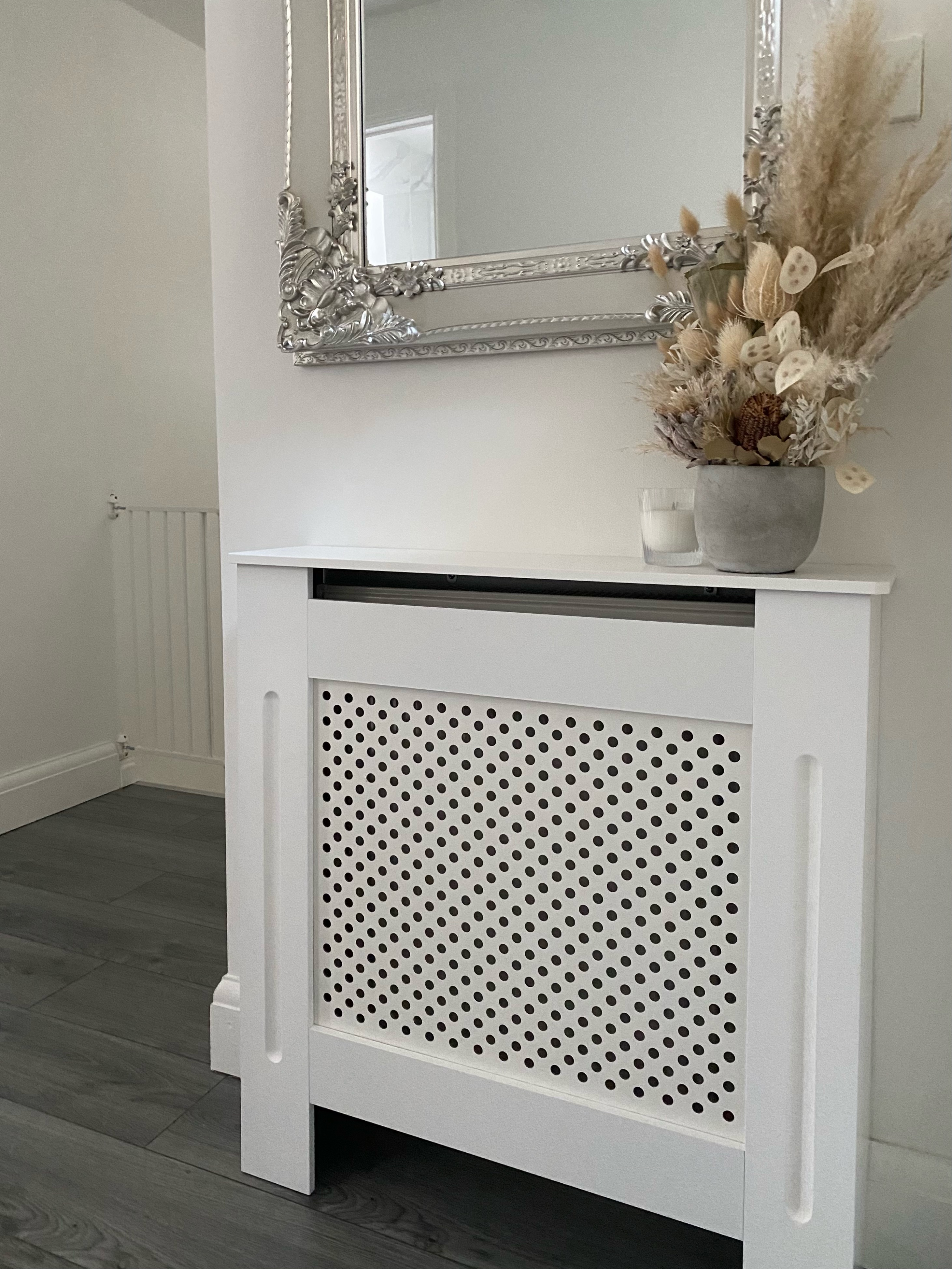Una copertura bianca per termosifone con fiori secchi e una candela.