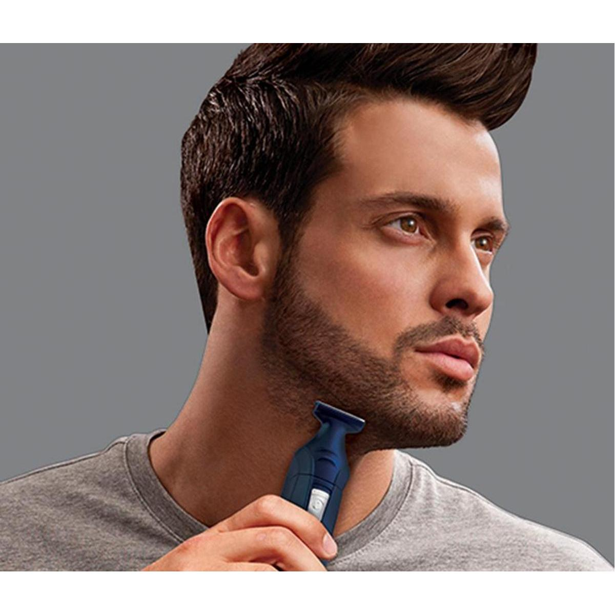 Man shaving his beard with a blue trimmer against a gray background.