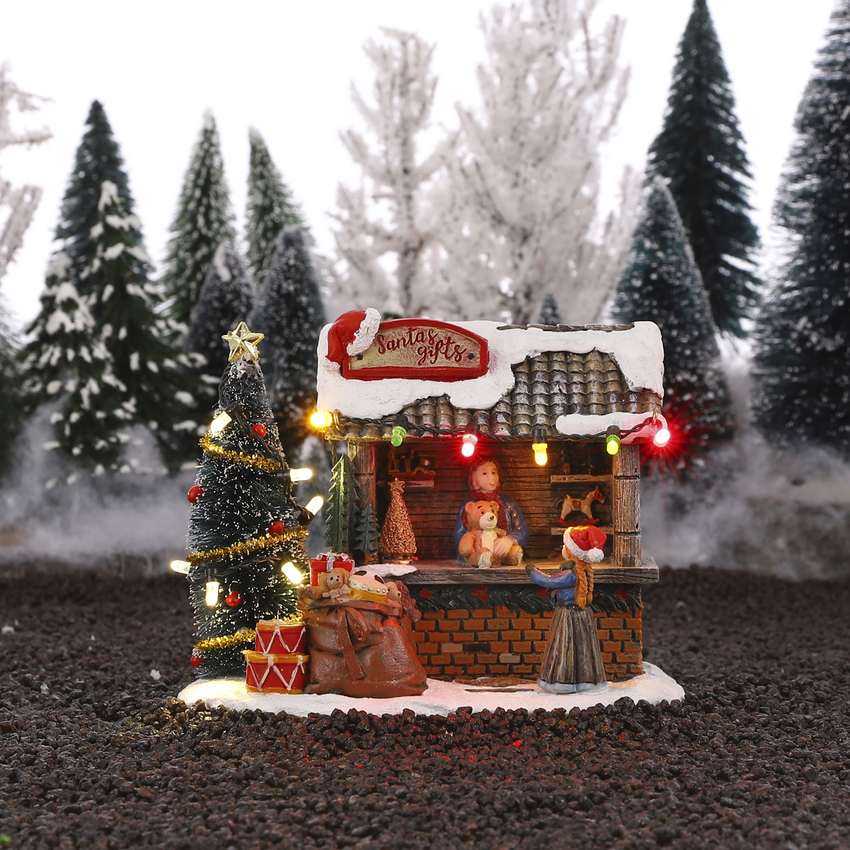 Een miniatuur kerstdorp scène met de "Santa's gifts" kraam, bomen en feestverlichting.