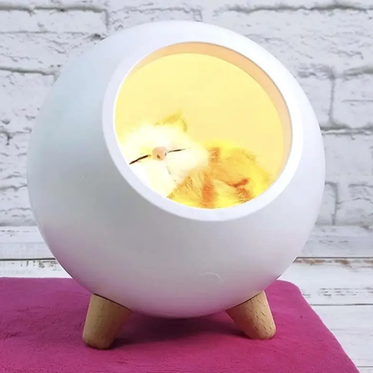 Eine flauschige orange-weiße Katze schläft in einem weißen, kugelförmigen Haustierbett mit Holzbeinen.