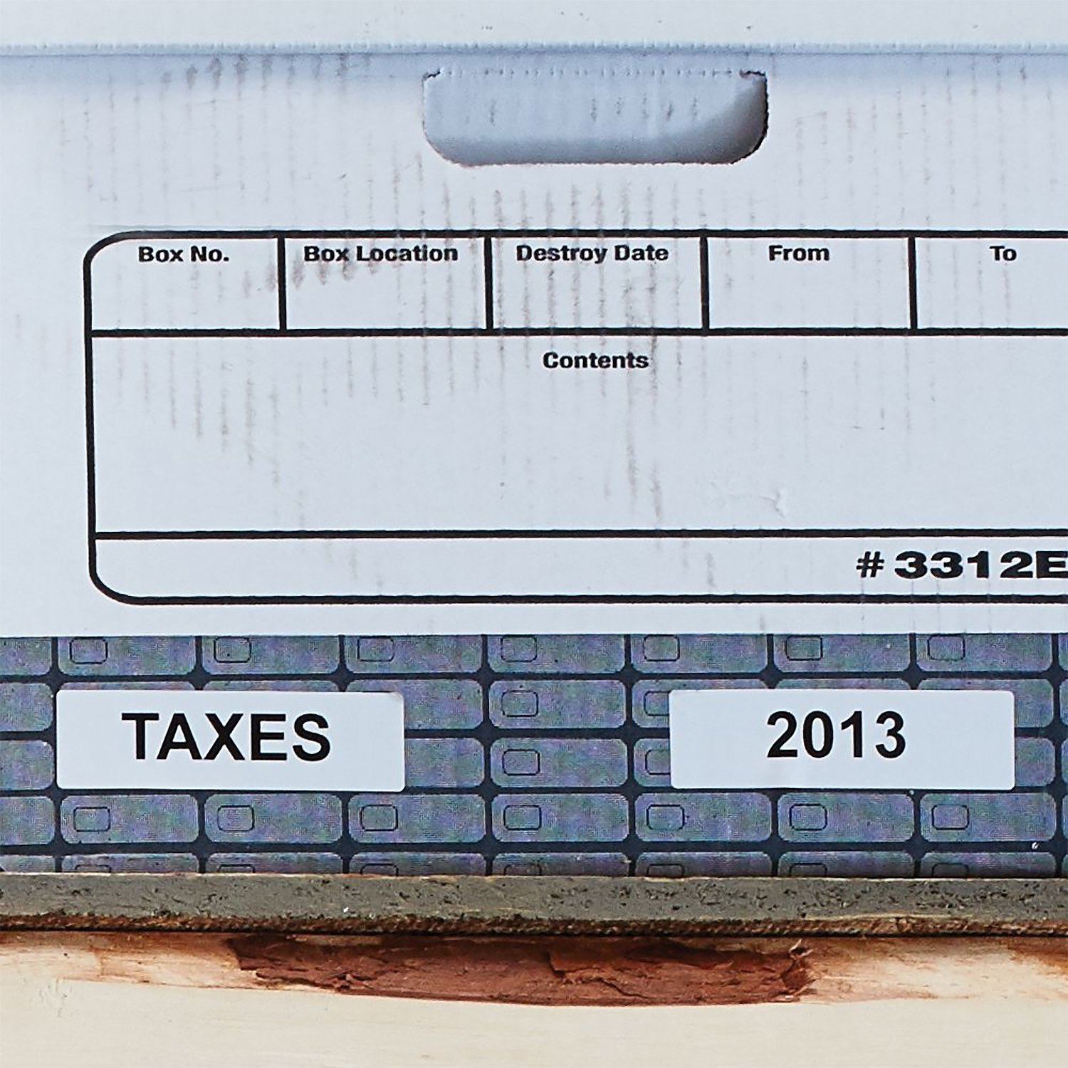Scatola di cartone con etichette 'TAXES' e '2013' su sfondo grigio testurizzato.