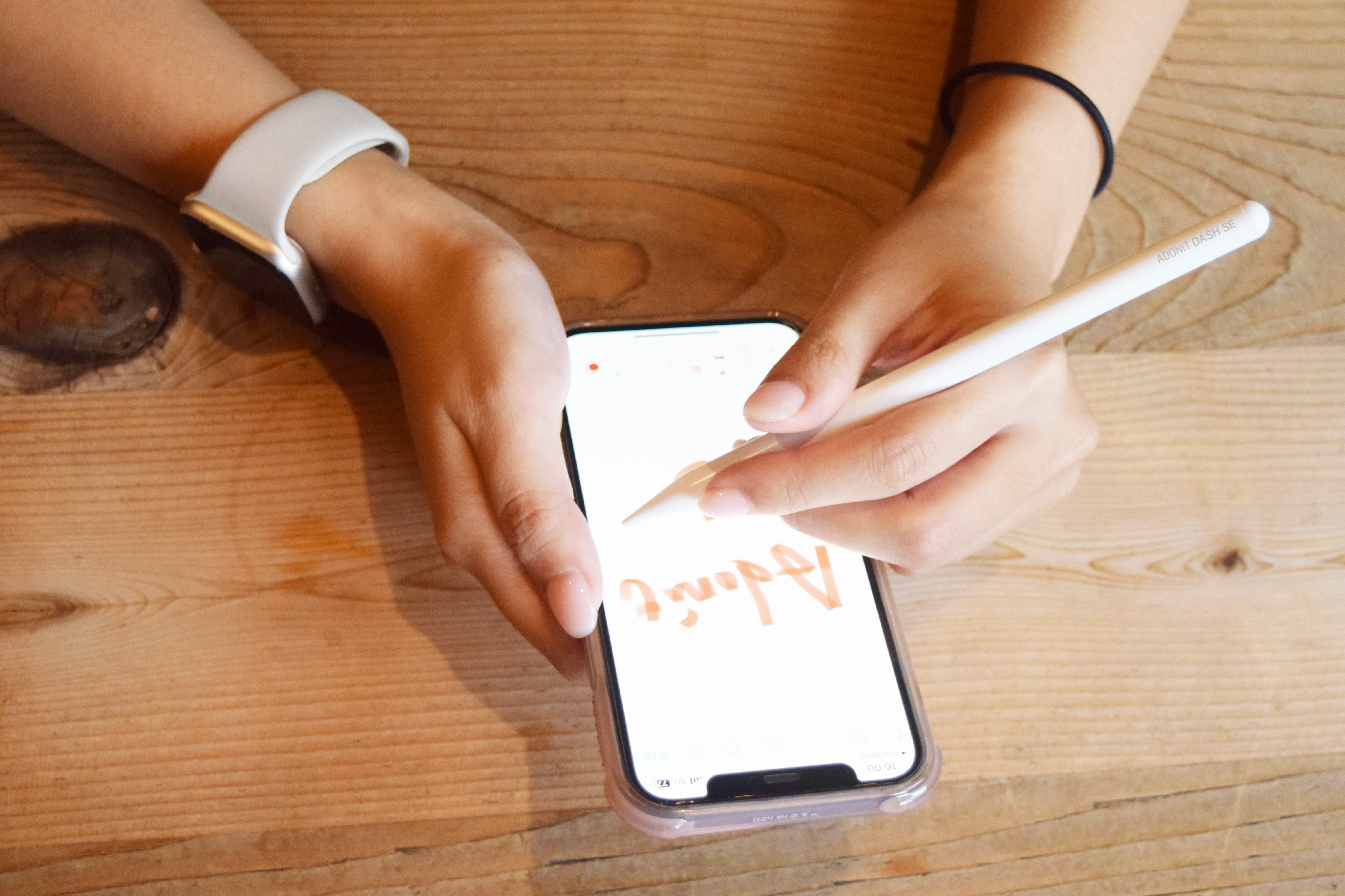 Mani che scrivono su un telefono con uno stilo su un tavolo di legno.