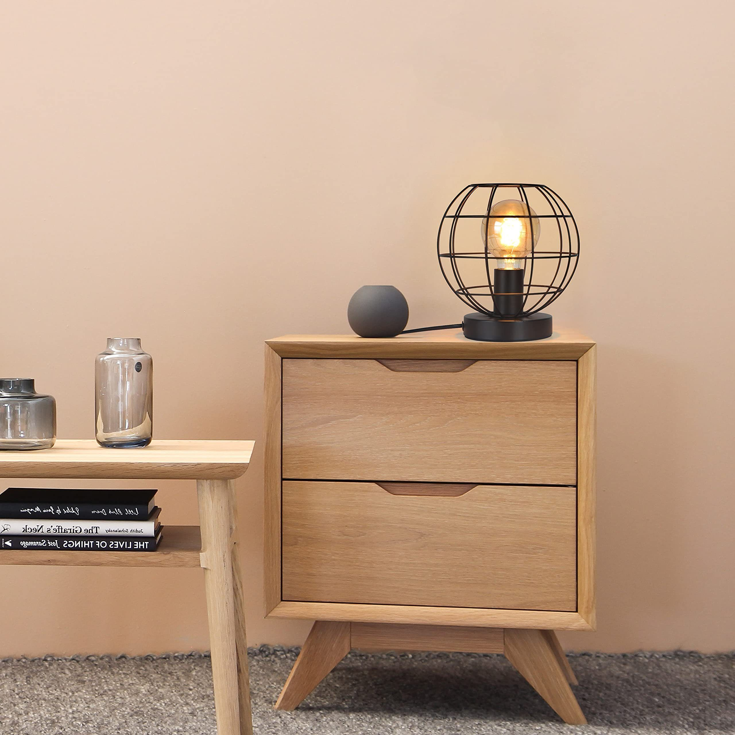 Comodino in legno con due cassetti, lampada, vaso e libri.