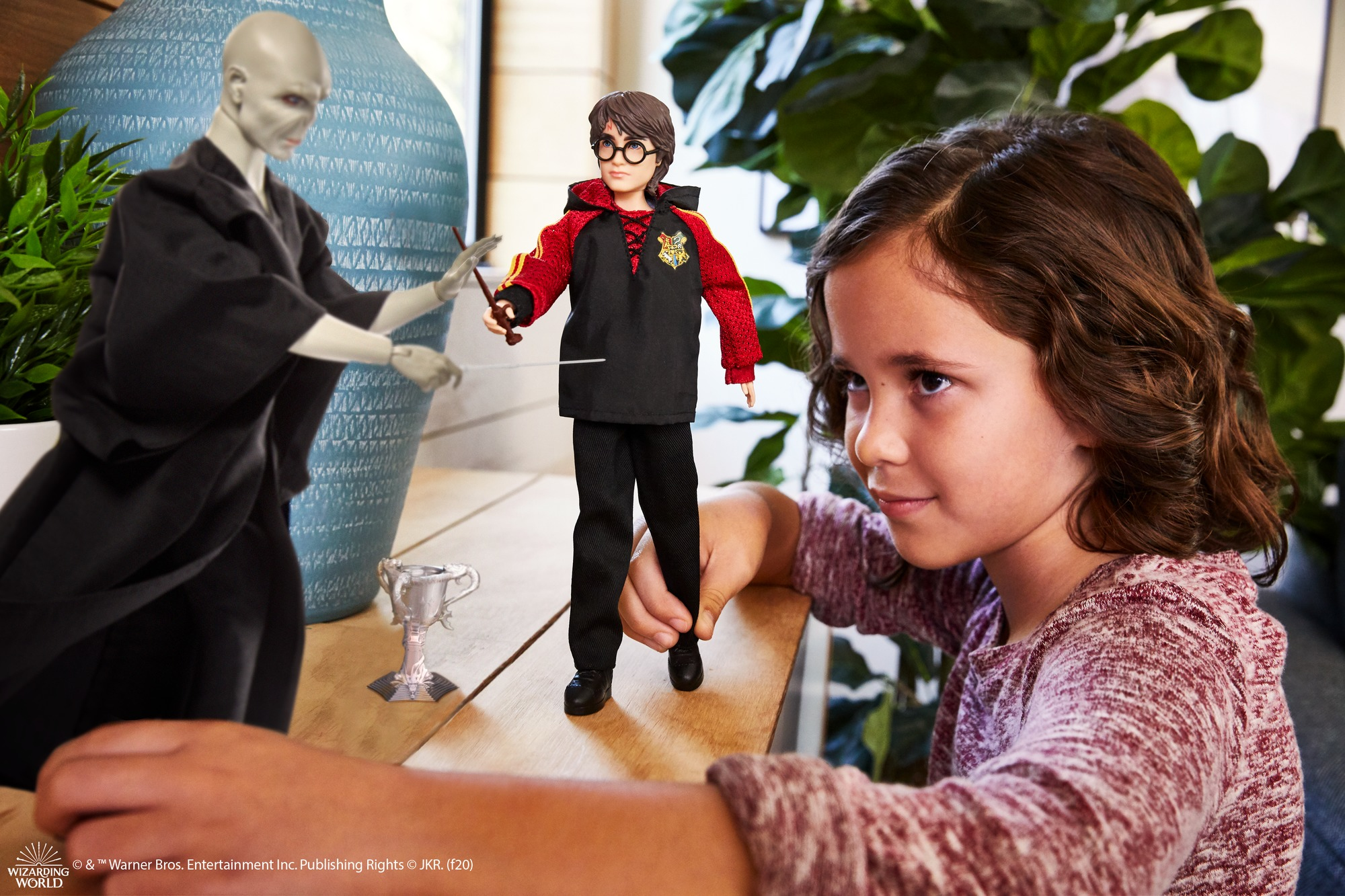 Bambina gioca con bambole Harry Potter e Voldemort vicino trofeo su tavolo legno.