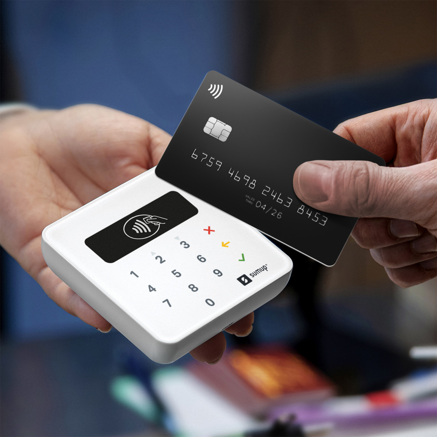 Una carta di credito nera con simbolo contactless viene avvicinata a un terminale di pagamento SumUp bianco.
