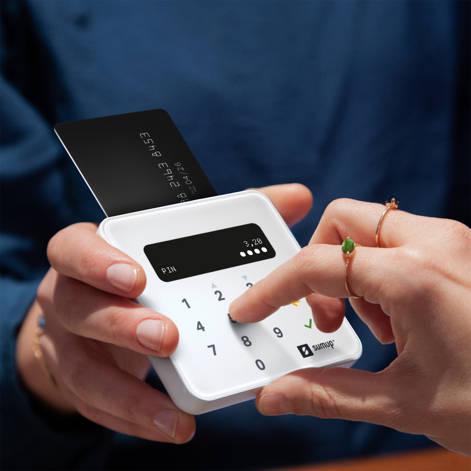 Una persona inserisce una carta di credito nera in un terminale di pagamento SumUp bianco mentre digita un PIN.