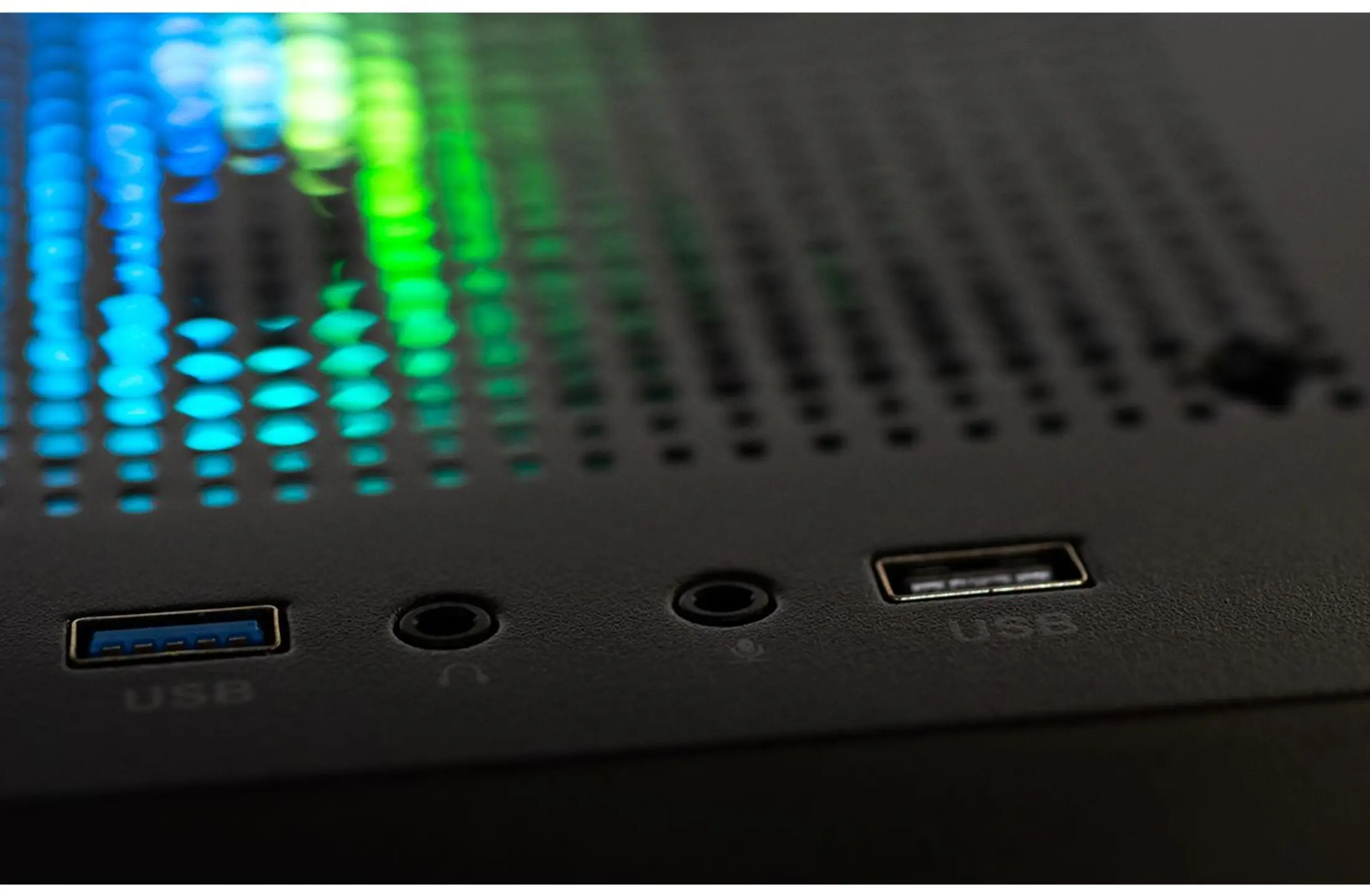 Close-up van een zwarte computerkast met USB-poorten en audio-aansluitingen. Wazige RGB-lampjes gloeien.