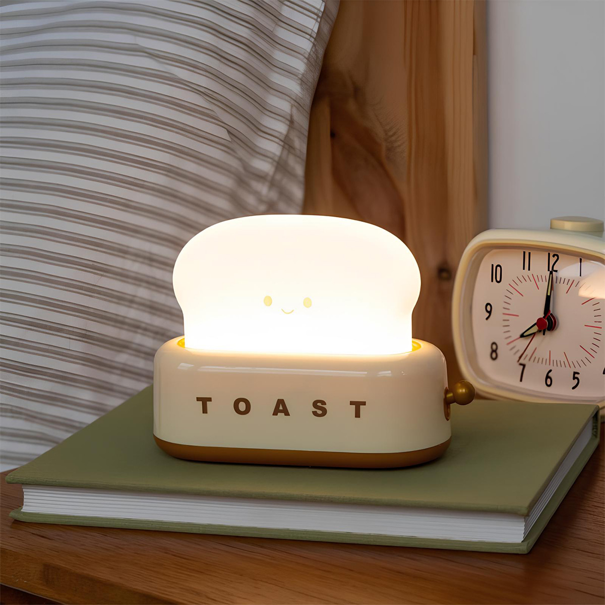 Eine süße Toast-förmige Lampe mit einem lächelnden Gesicht sitzt auf einem Buch neben einem Wecker.