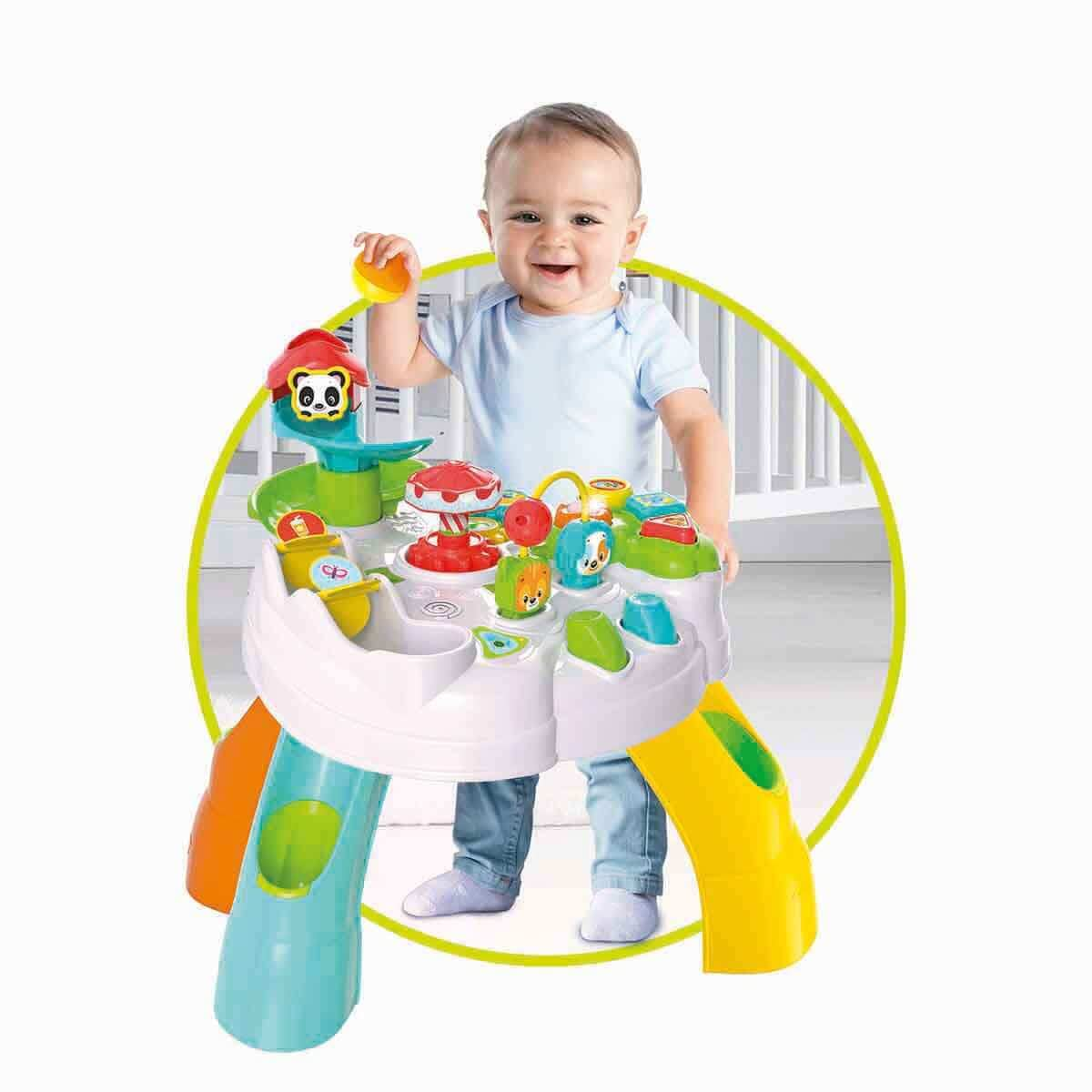 Mavi tişörtlü ve kot pantolonlu gülen bir bebek, renkli aktivite masasıyla oynuyor.
