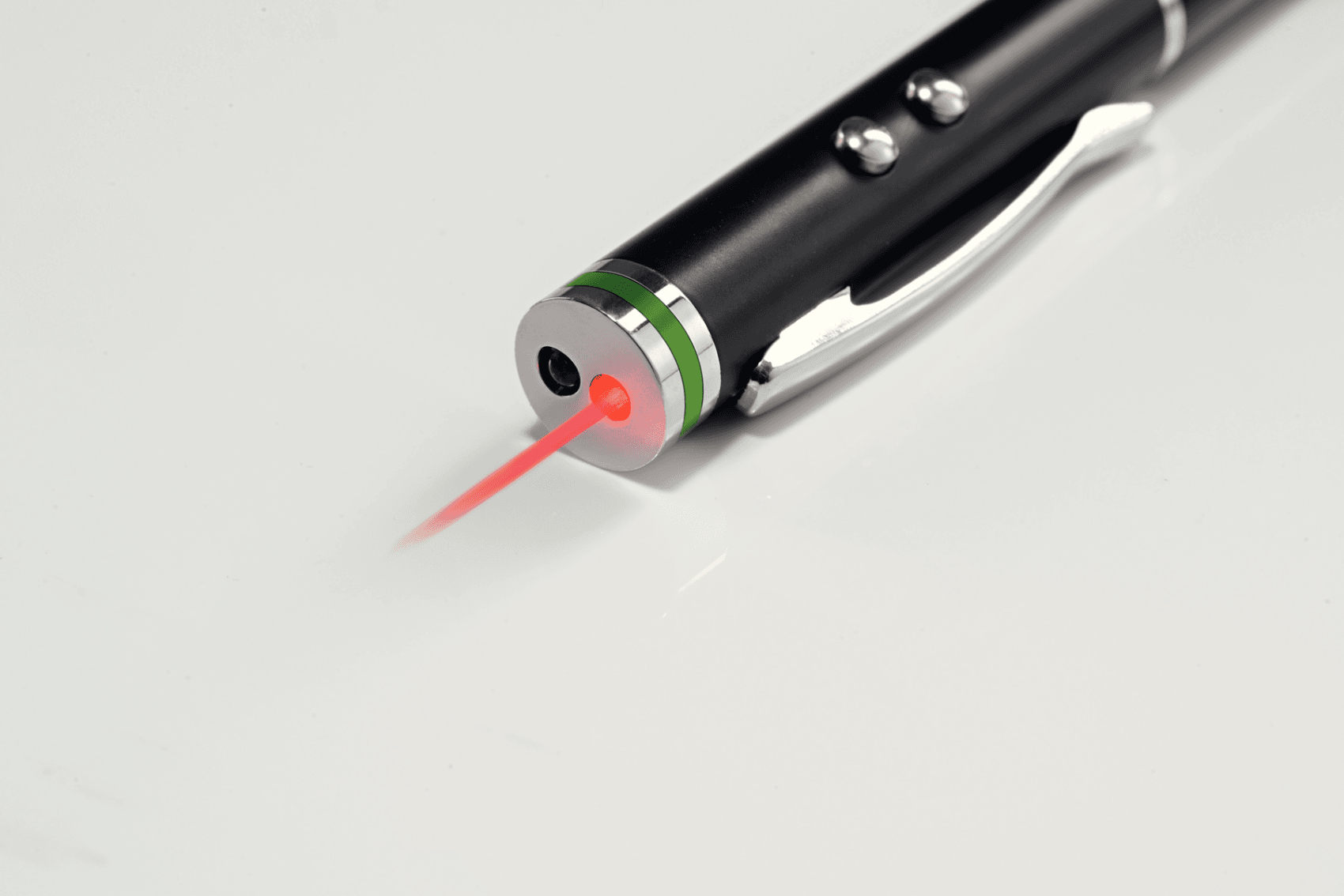 Un puntatore laser nero con clip argentata emette un raggio laser rosso su una superficie bianca.