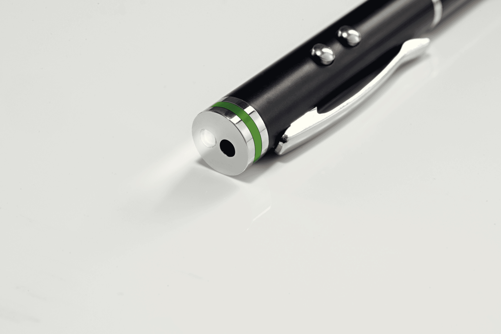 Puntatore laser nero con clip argentata e accenti verdi su superficie bianca.